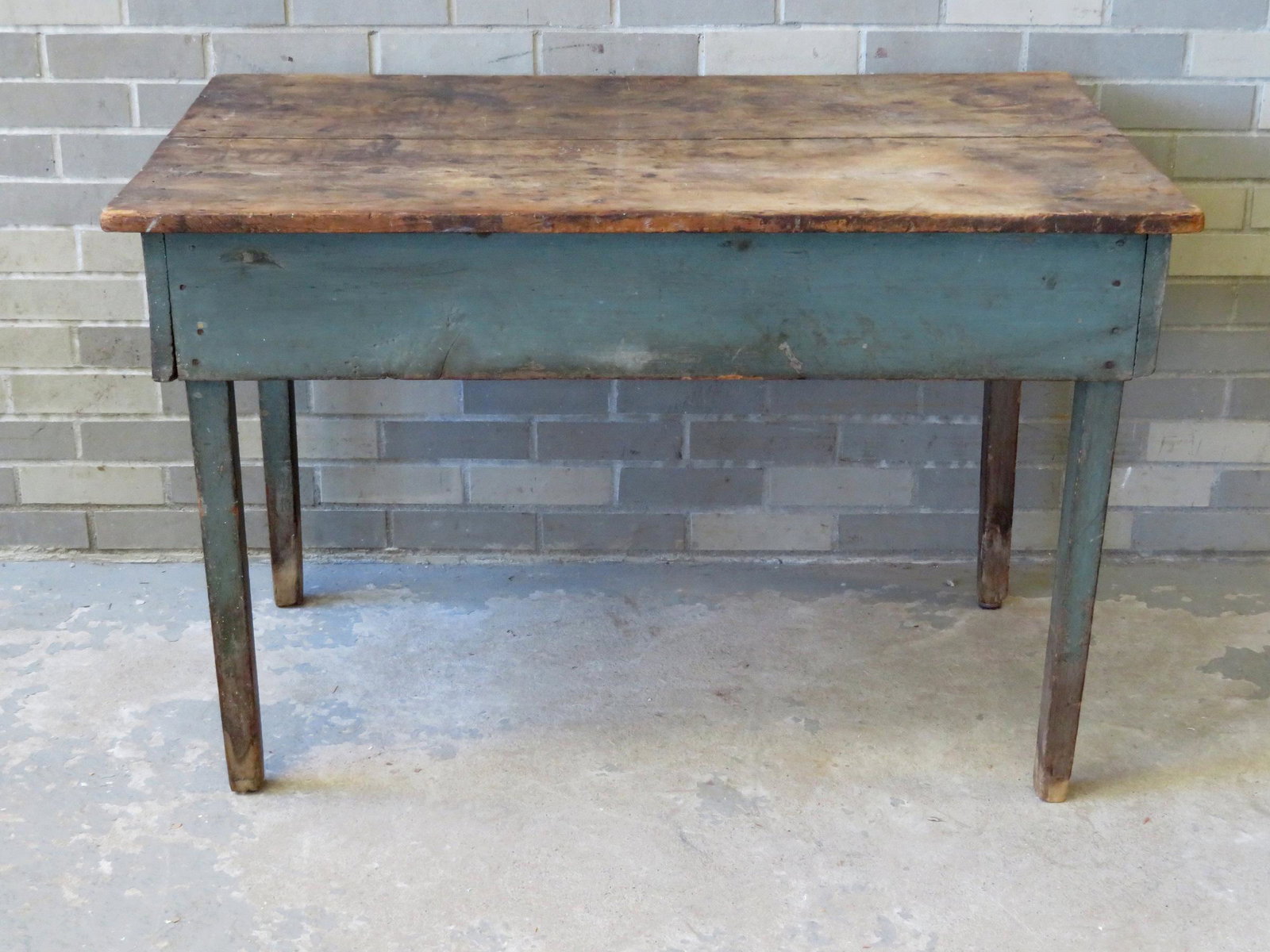 A primitive tapered leg work table with scrubbed top: A primitive tapered leg work table with scrubbed top and apron and legs in original blue/green paint, early 19th century. Square nail construction. 43 1/4"W x 27 1/8"D x 28"H. The top with staining, b