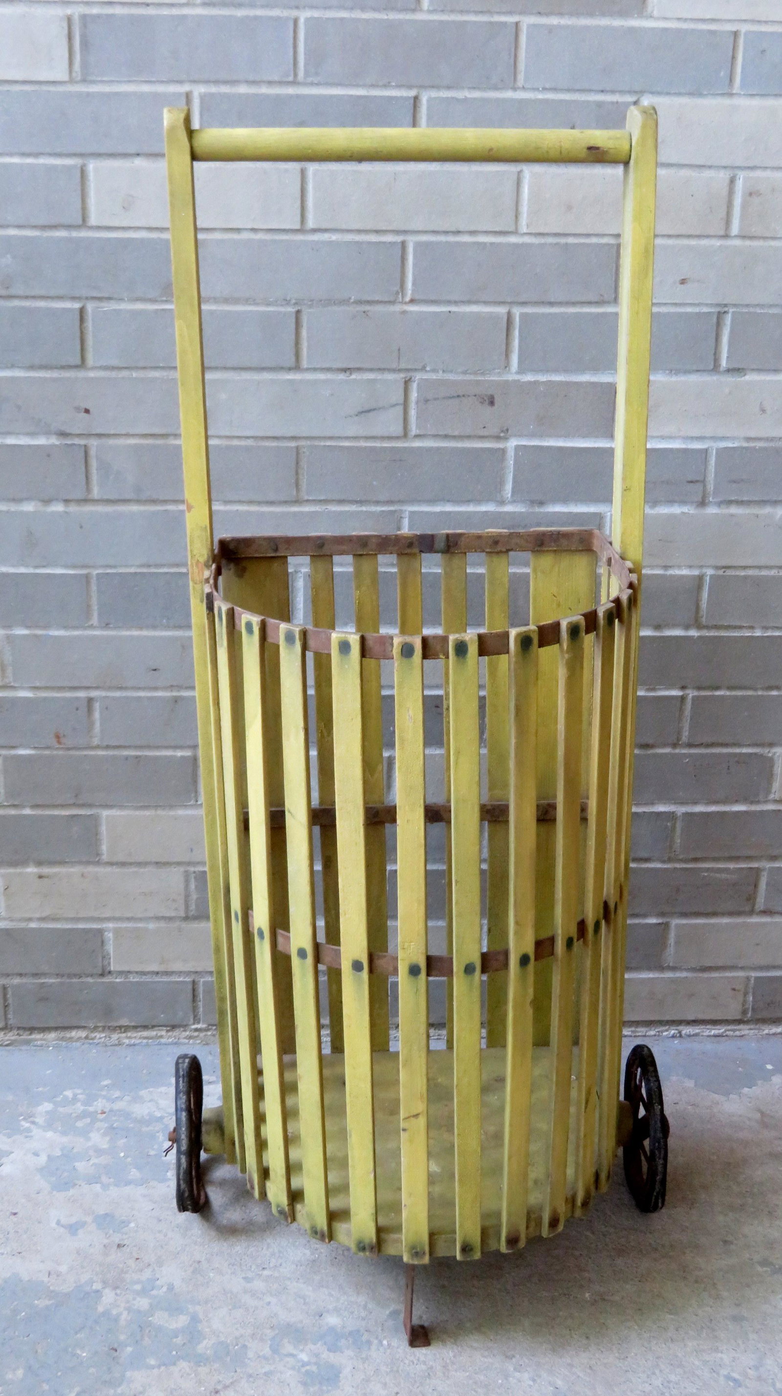 A vintage wooden grocery cart in original mustard paint: A vintage wooden grocery cart in original mustard paint and having rubber tires applied to star shaped metal wheels, and slated cage-like construction. Late 19th to early 20th century. 19"W x 12"D x 4