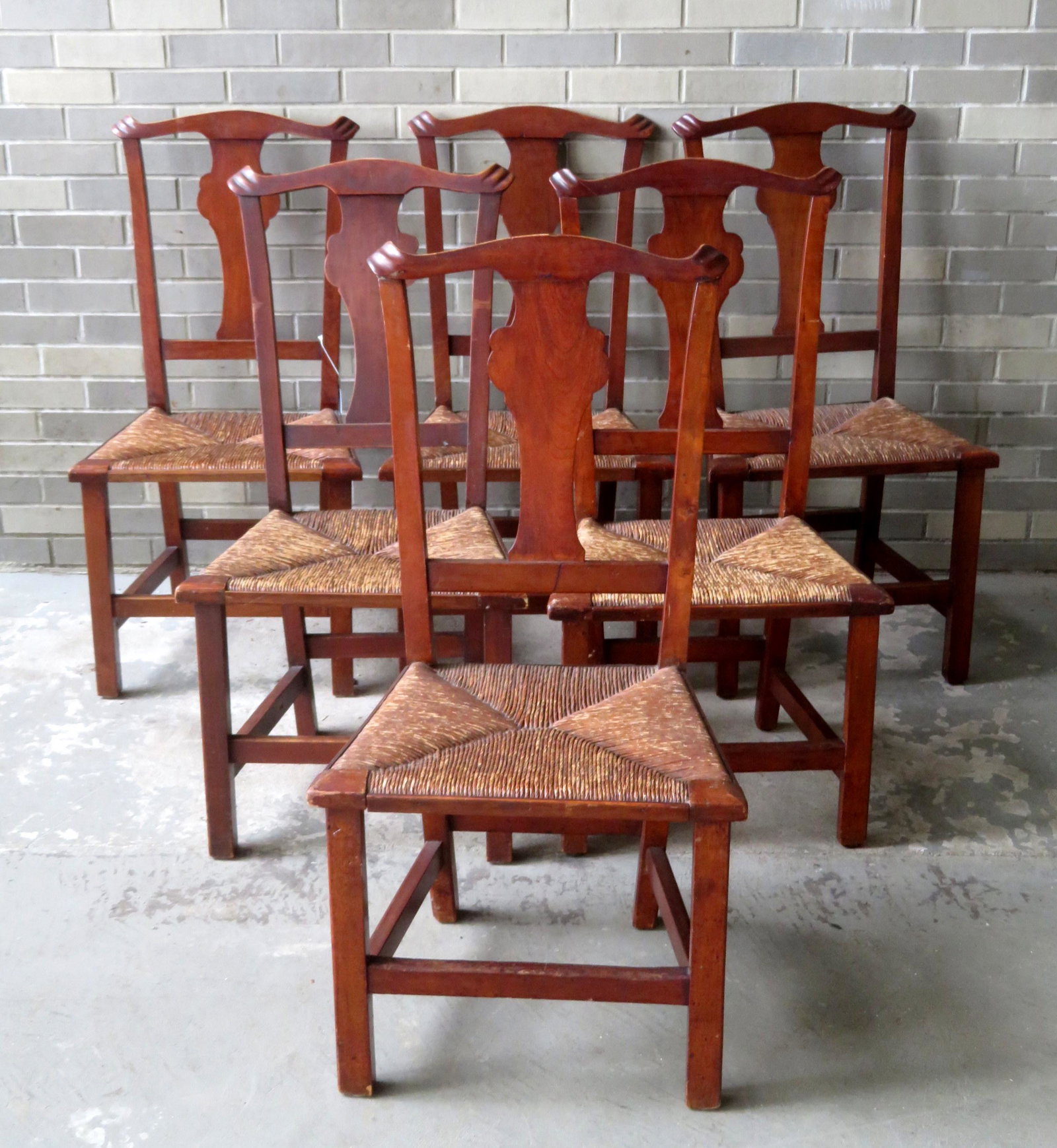 A set of 6 matching country Chippendale chairs in: A set of 6 matching country Chippendale chairs in cherry wood, with rush seats, carved ears, and slight chamfering on interior of the square legs. Traces of original red stain. Minor use wear througho