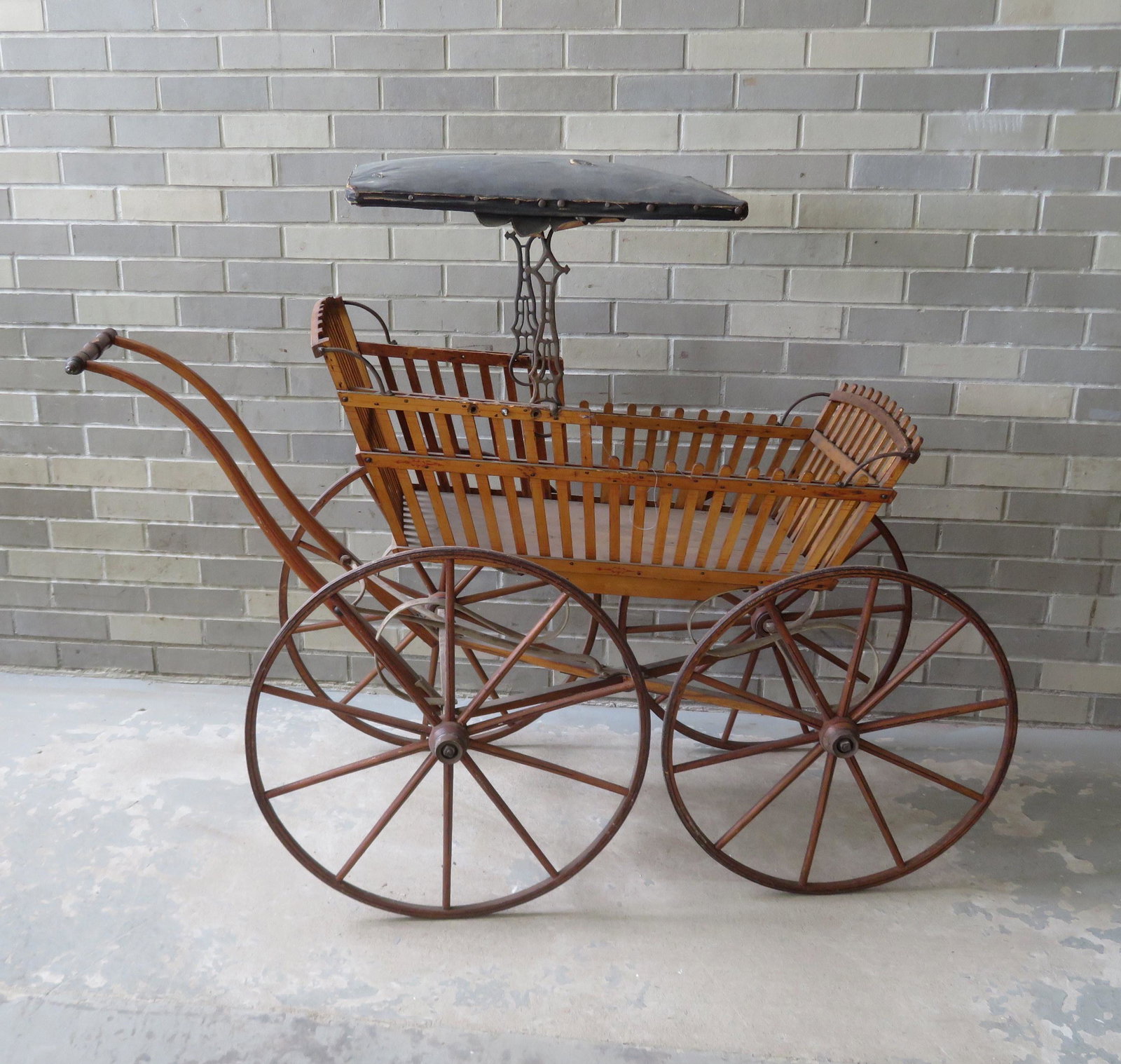 A 19th century country baby carriage with wooden slats: A 19th century country baby carriage with wooden slats with some stencils, wooden wheels with pin striping, and detachable leather canopy. Measures 54"L x 24"W x 35 1/2"H (excluding canopy). Missing t