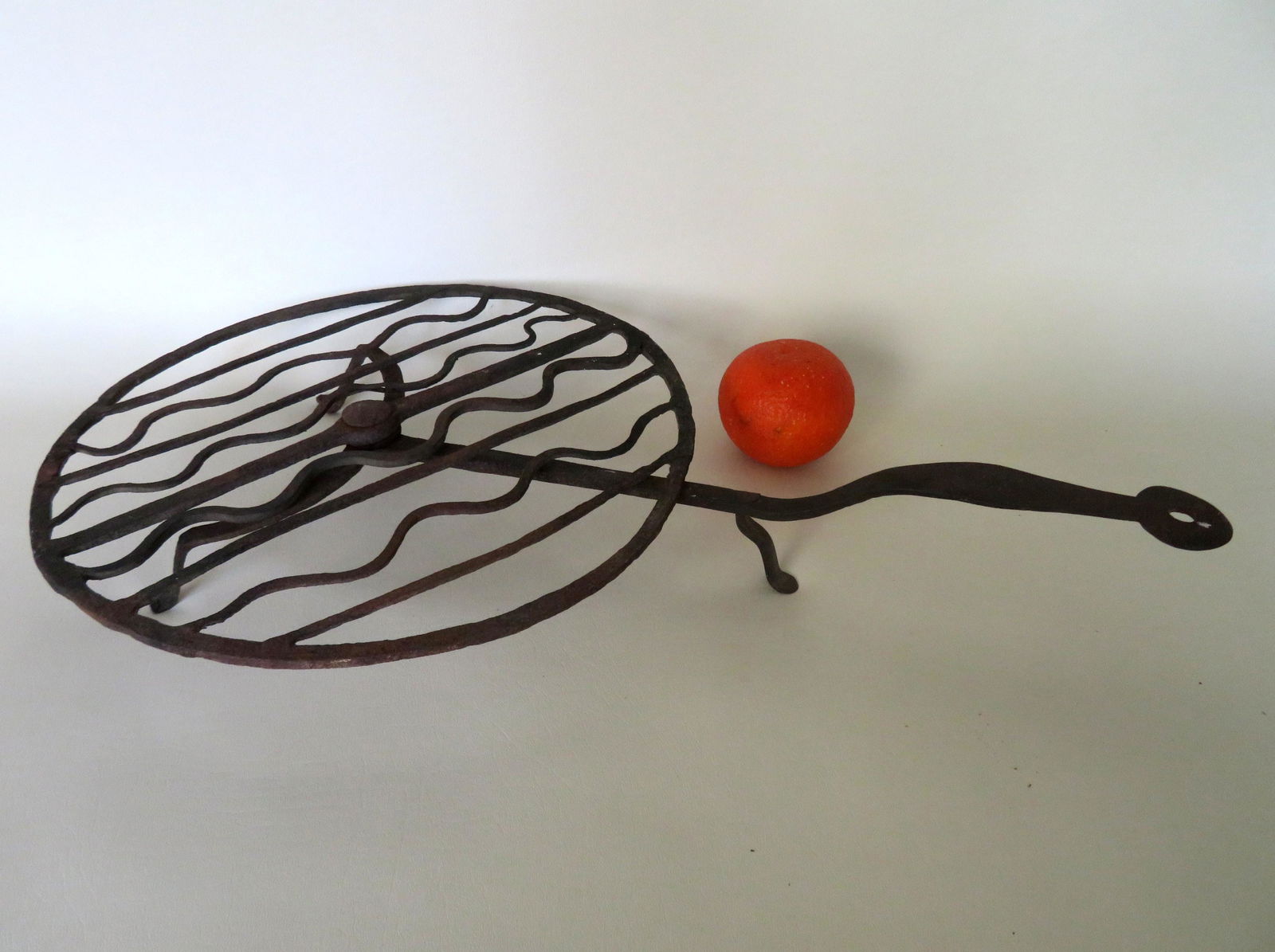 Hand forged iron hearth trivet with a revolving: Hand forged iron hearth trivet with a revolving circular top with 4 straight and 4 wavy bars seated on 3 legs with slightly rounded feet, 18th century. 12 3/4"D x 22"L x 2 3/4"H. Very good condition.