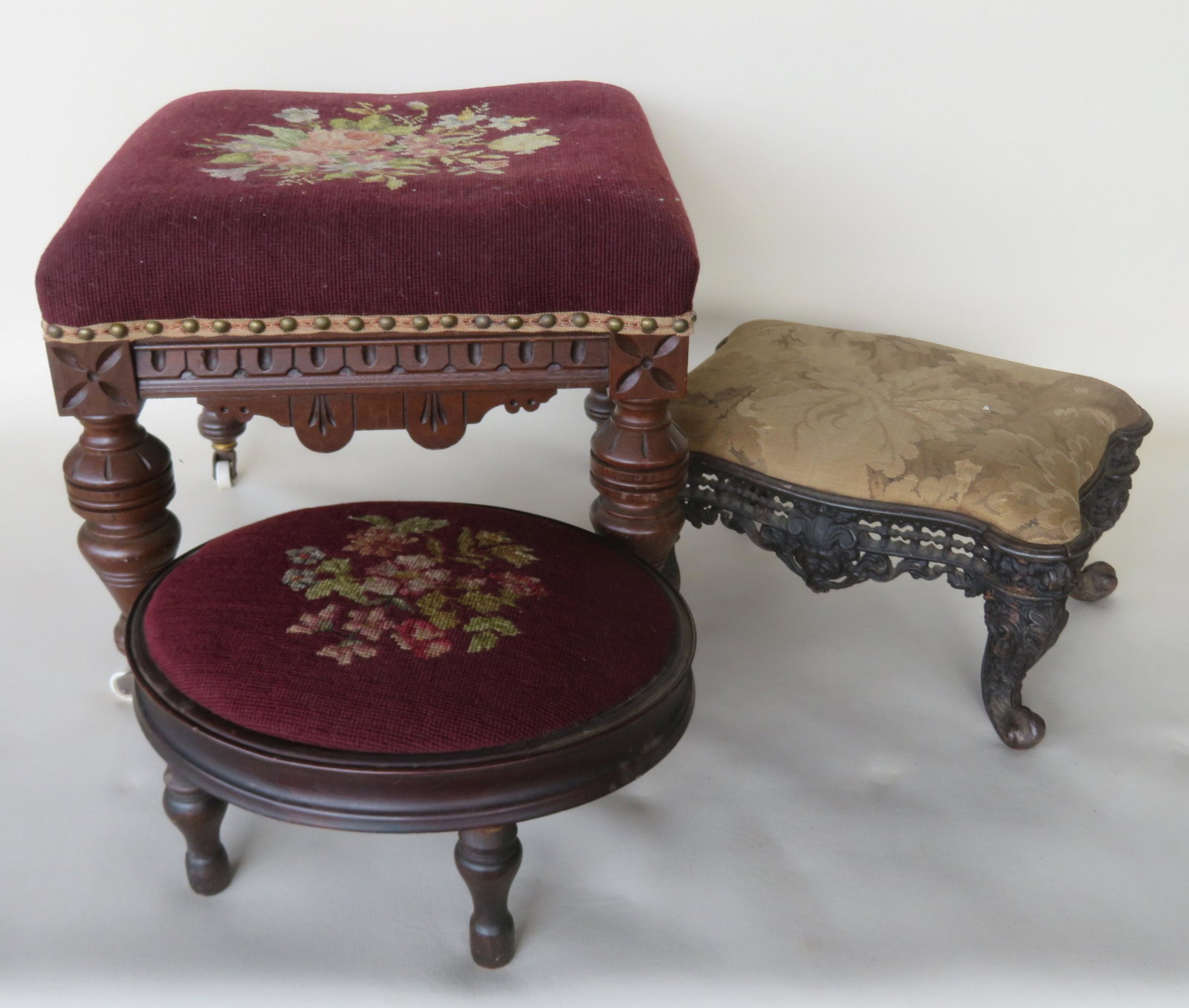 Three Victorian upholstered footstools including: The: Three Victorian upholstered footstools including: The first chip carved black walnut with needlepoint seat and turned legs leading to casters, very good condition, late 19th century, 16 1/2" square x 
