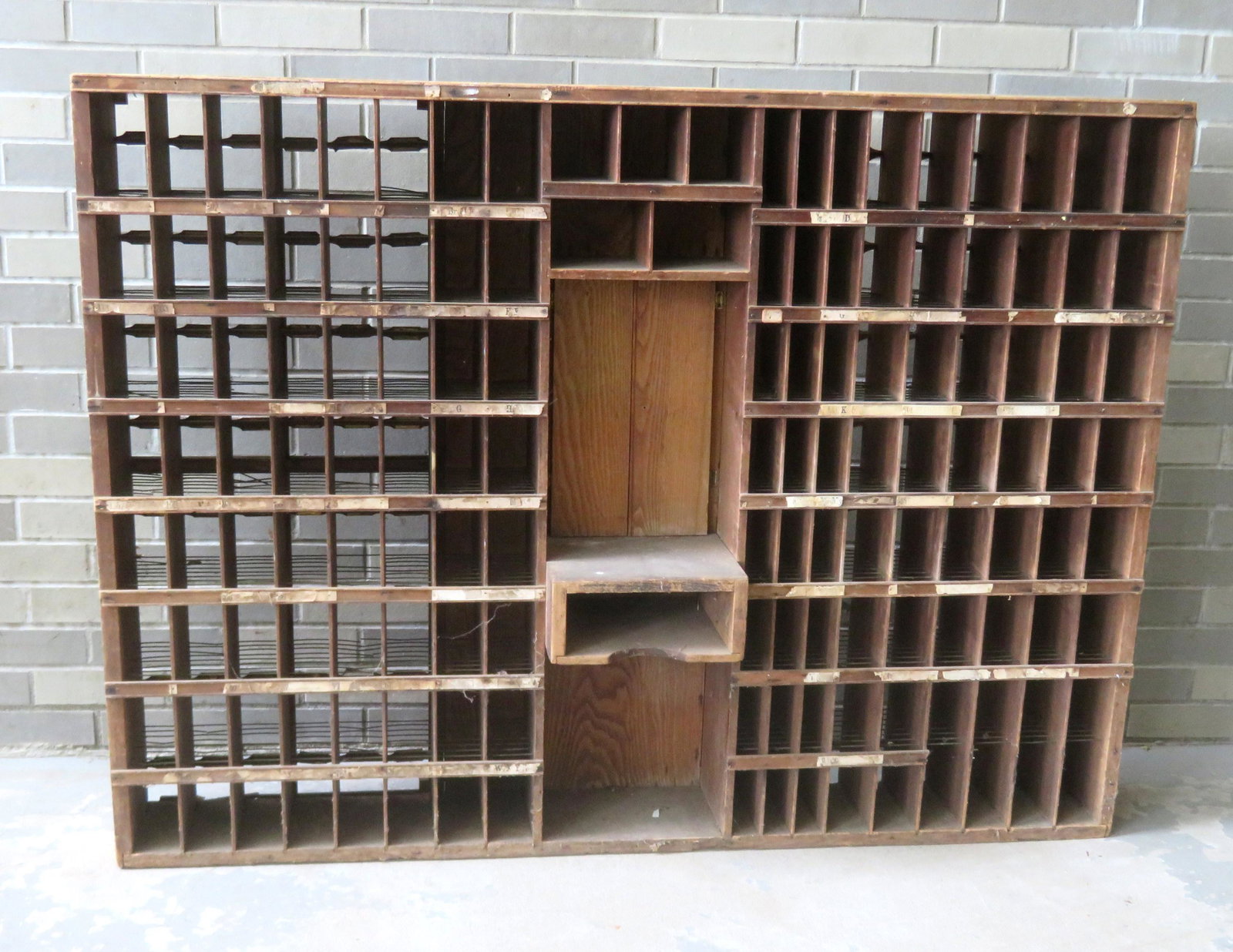 A US oak postal box unit originally attached to a: A US oak postal box unit originally attached to a counter top, consisting of numbered cubby hole units surrounding the central postal clerk's counter with swing open doors. Below the opening is a mail