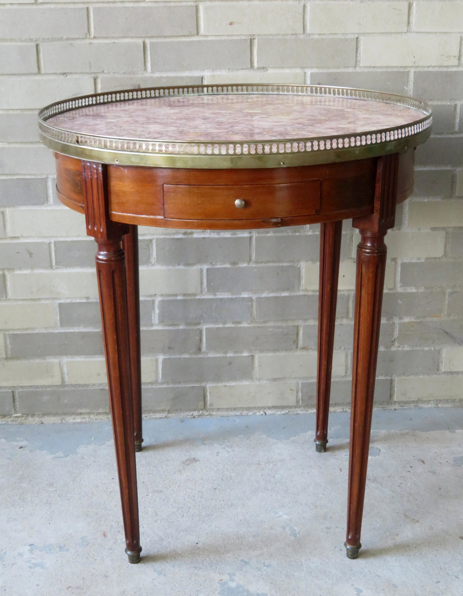 A circular Louis XVI style gueridon with marble inset,: A circular Louis XVI style gueridon with marble inset, brass gallery, 2 end drawers, 2 pullout candle surfaces, and having tapered and fluted legs, early 20th century. 25 1/4"Dia. x 29 3/8"H. Several 