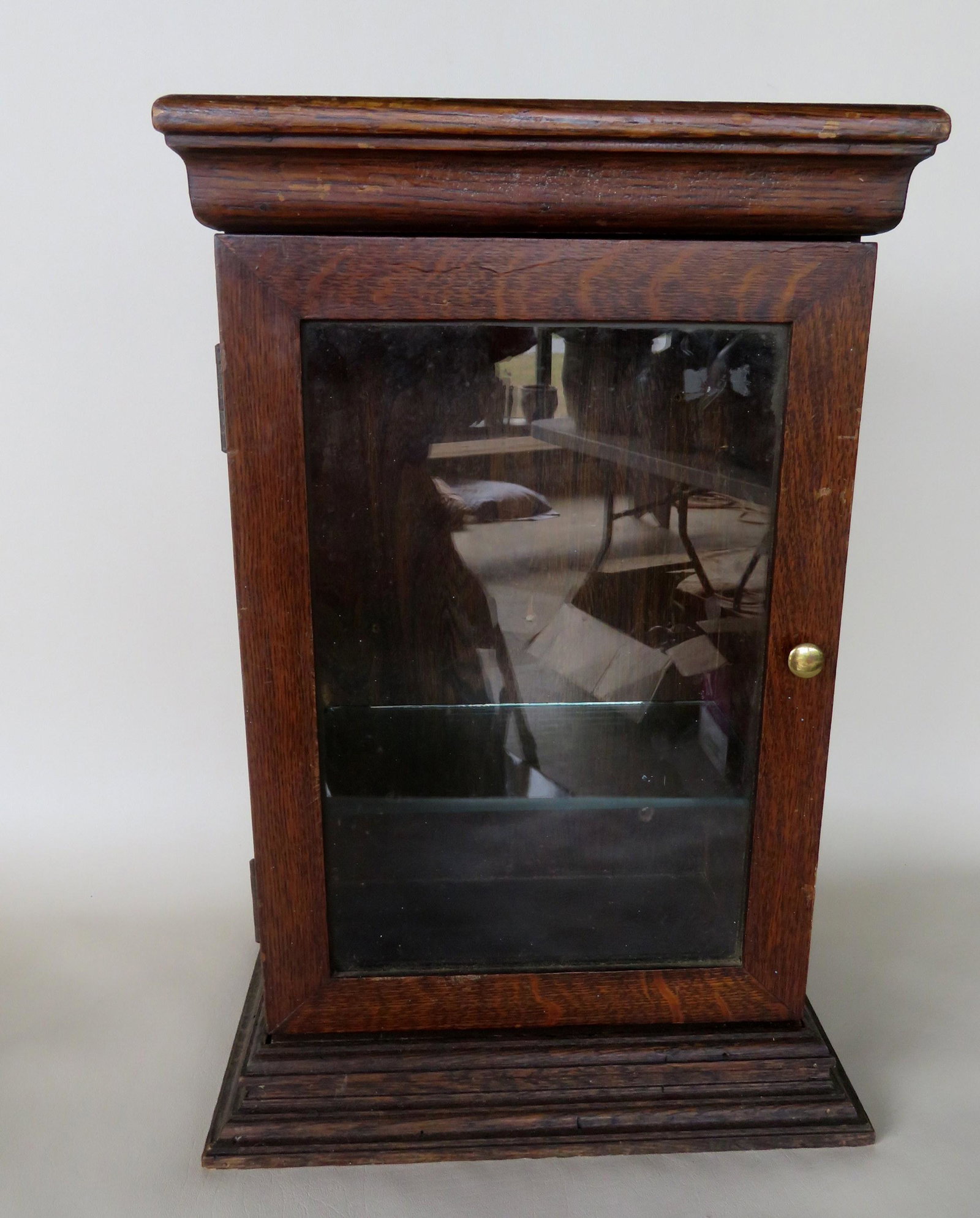 An oak wall cabinet with a single glass door and: An oak wall cabinet with a single glass door and stepped molding on base, late 19th century, original finish, very good condition. 13 3/4"W x 9"D x 21 1/2"H.