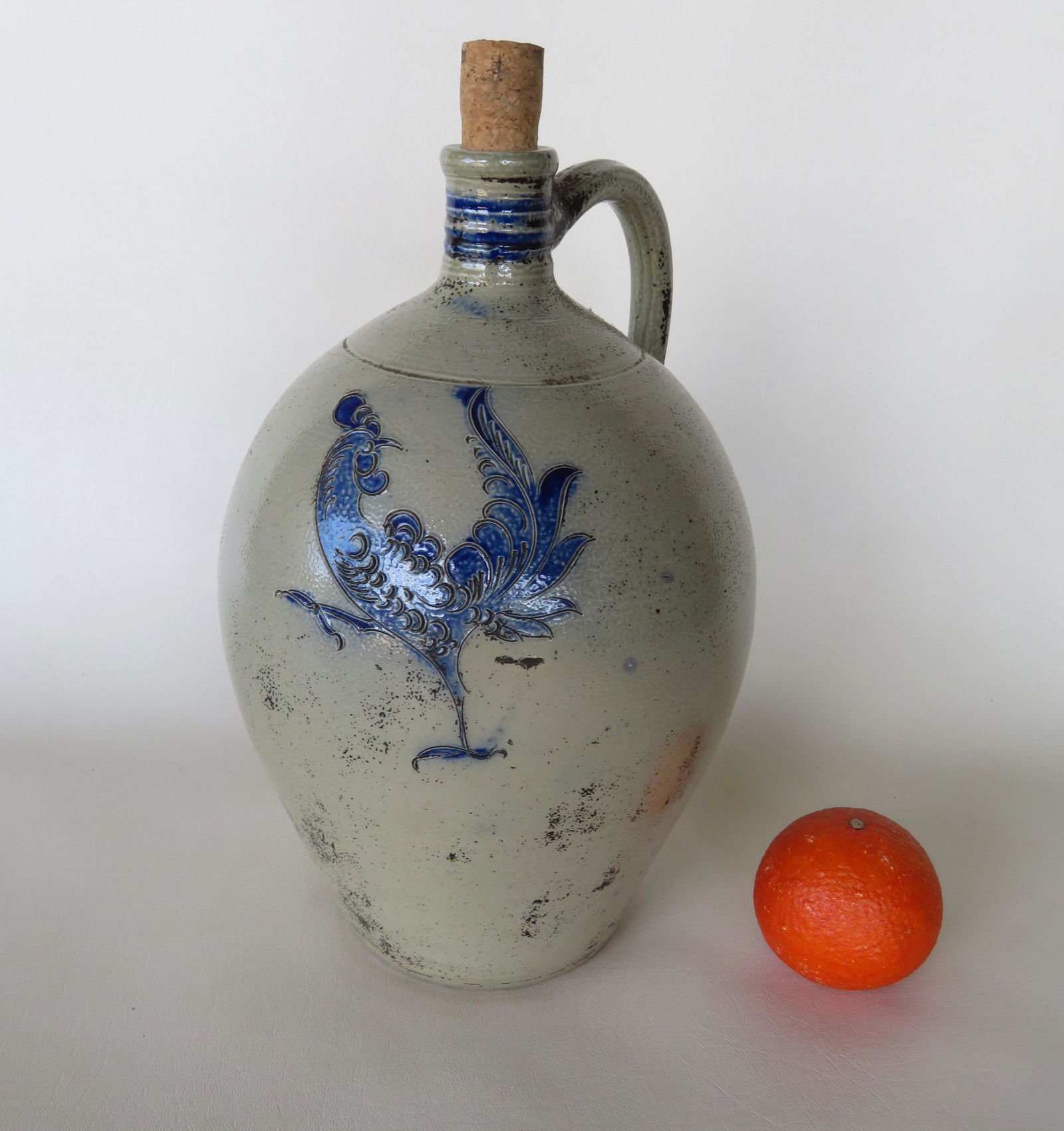 Stoneware ovoid crock, decorated with an incised: Stoneware ovoid crock, decorated with an incised strutting rooster brushed in cobalt blue as well as incised heart shaped flowers flanking the narrow and tooled handle. The jug also with a tooled neck