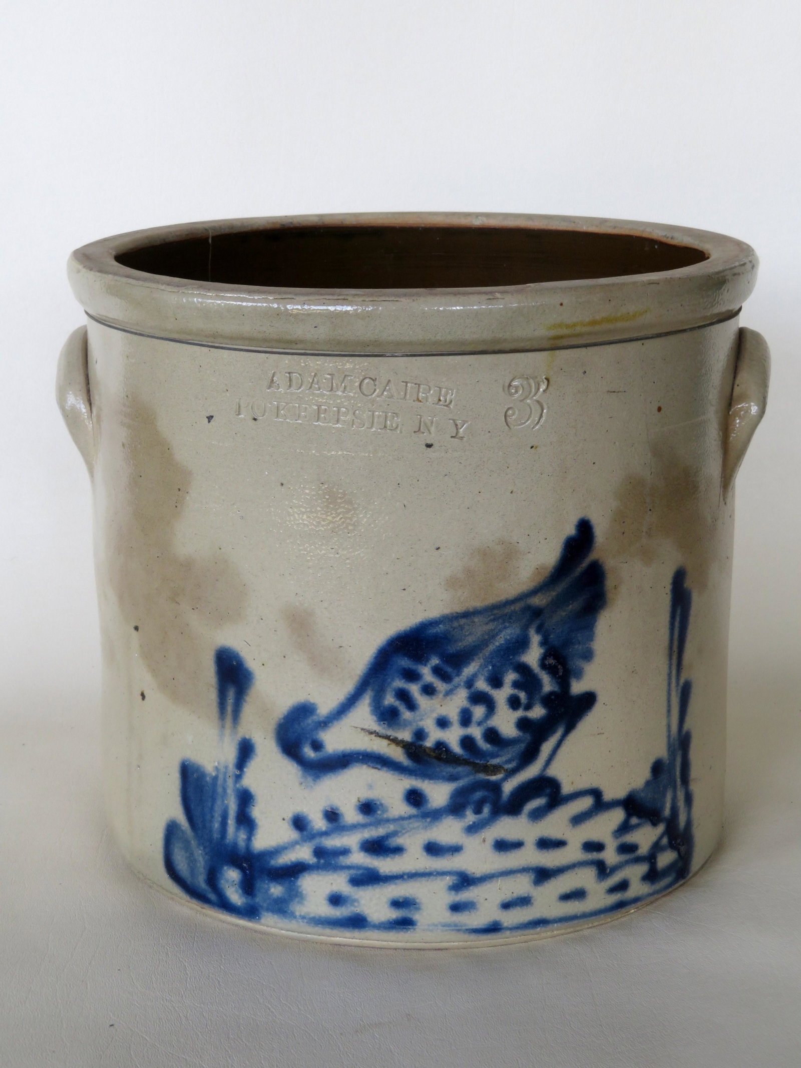 Stoneware crock with impressed mark of "Adam Caire /: Stoneware crock with impressed mark of "Adam Caire / Pokeepsie NY", 3 gallon size, decorated with a deep cobalt blue chicken pecking corn between floral stems. Some light staining, 2 hairline cracks, 