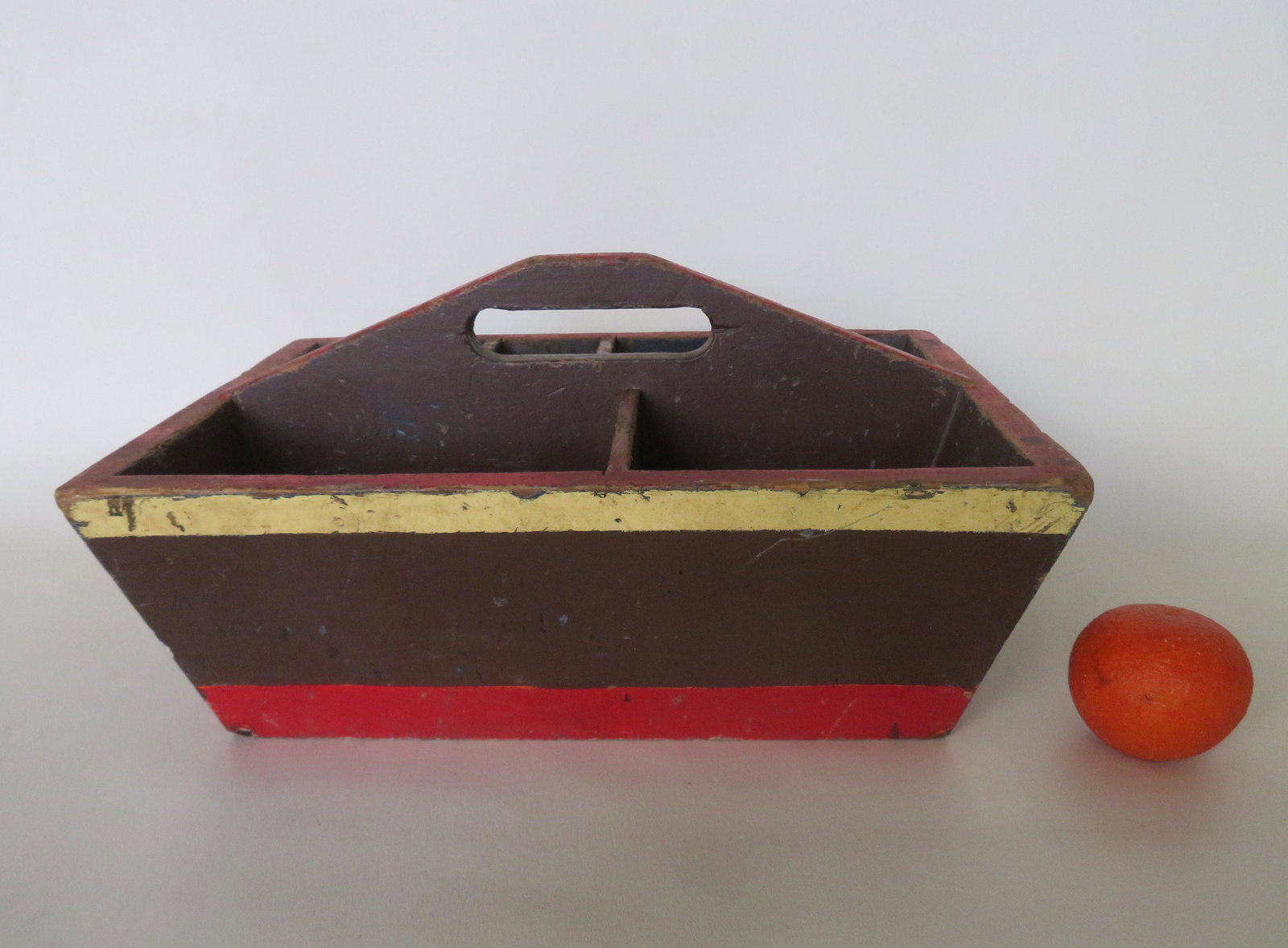 A primitive tool carrier with sectioned interior, in: A primitive tool carrier with sectioned interior, in old brown paint with yellow and red bandings around perimeter over original blue. 19th century. Good condition. 17"W x 13 1/4"D x 8 1/2"H.