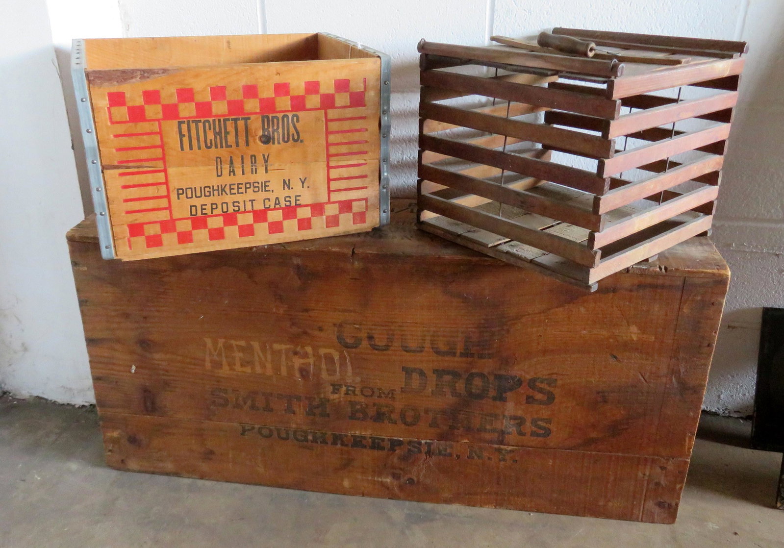 Three advertising crates including: A wooden egg crate: Three advertising crates including: A wooden egg crate carrier with bail handle, faintly signed "Humpty Dumpty"; a milk crate with red checkered design marked "Fitchett Bros. Dairy Poughkeepsie, N.Y."