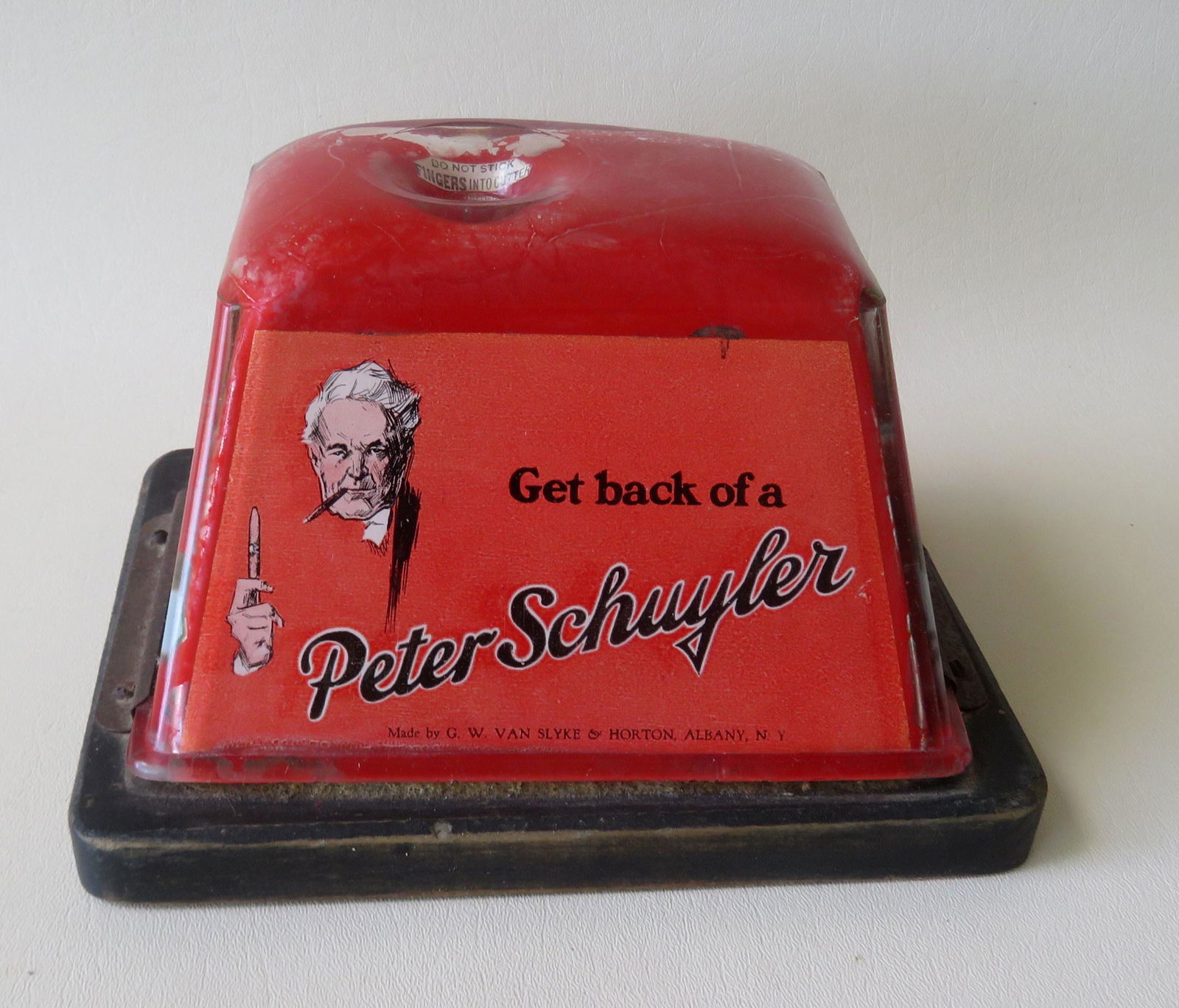 An automated advertising table top Peter Schuyler cigar: An automated advertising table top Peter Schuyler cigar cutter with glass case over original metal clockworks cutter, mounted on original wooden base. It has a windup key on reverse and is activated b