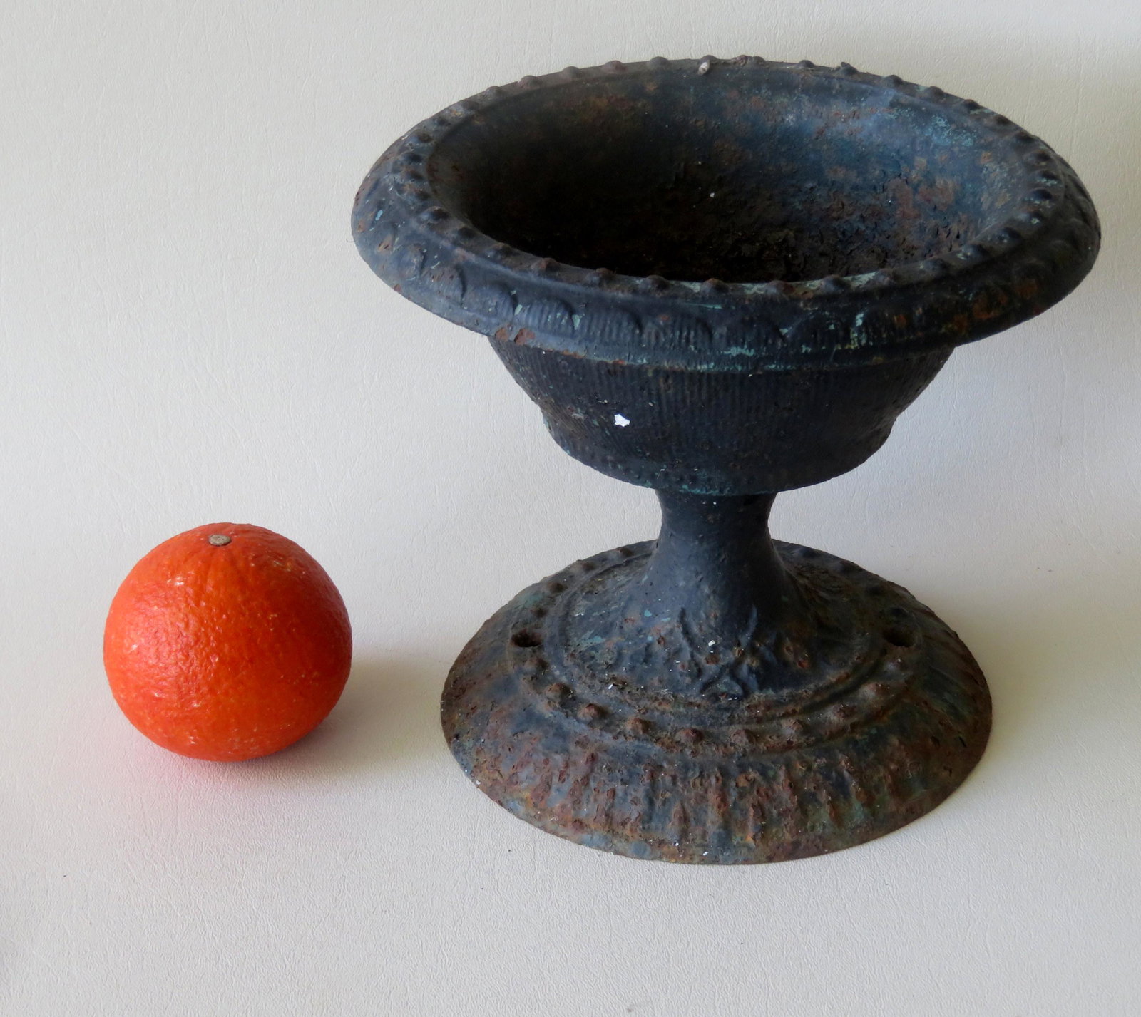 A small table top cast iron urn with embossed: A small table top cast iron urn with embossed decorations on rim and footed base, 19th century. Some surface rust, traces of old black paint, and in very good structural condition. 7 1/4"H x 8 5/8"D. 