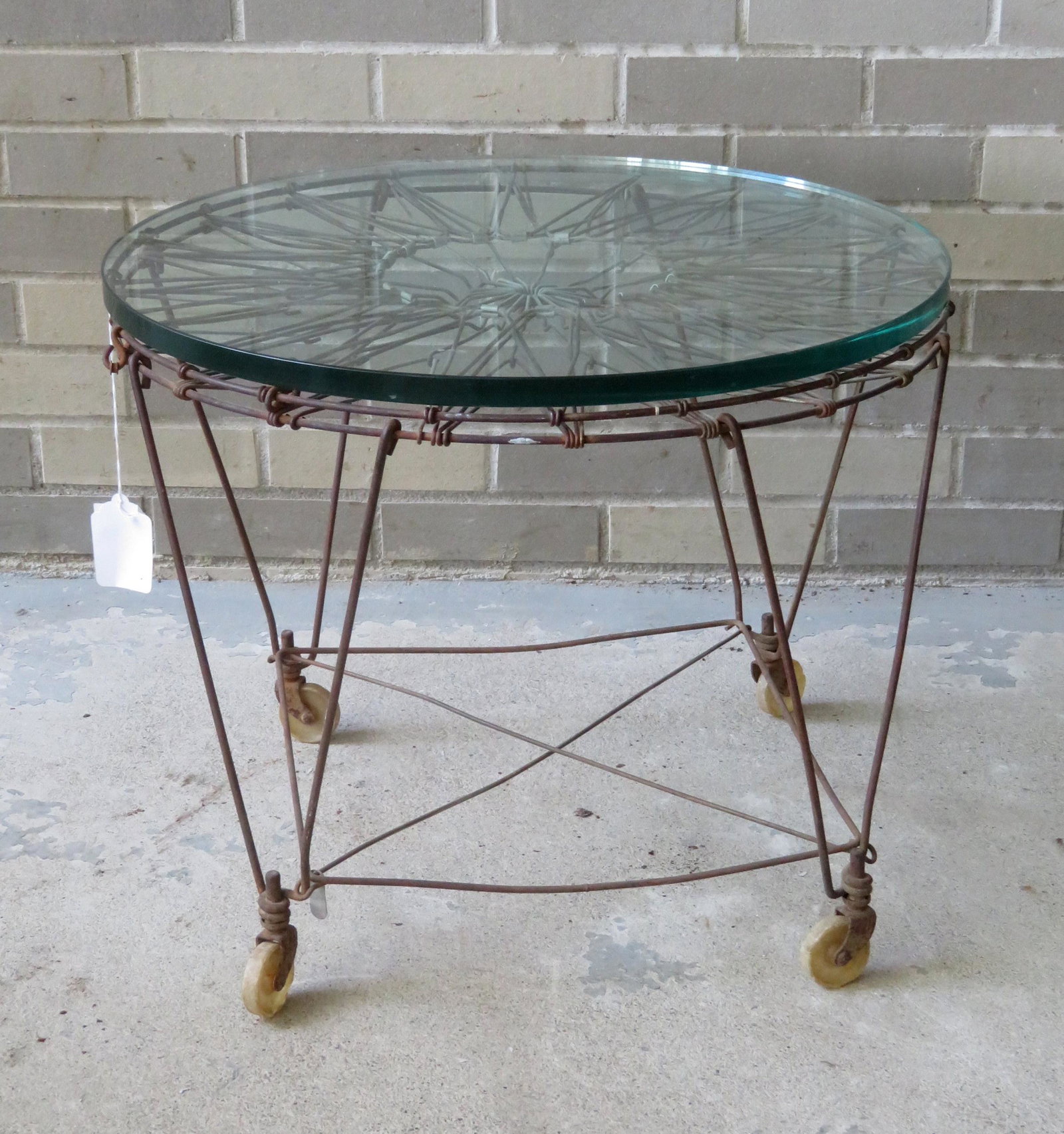 A floor standing wire laundry basket on wheels,: A floor standing wire laundry basket on wheels, collapsible, converted to end table with the application of a glass top. Very good condition. Circa 1950.