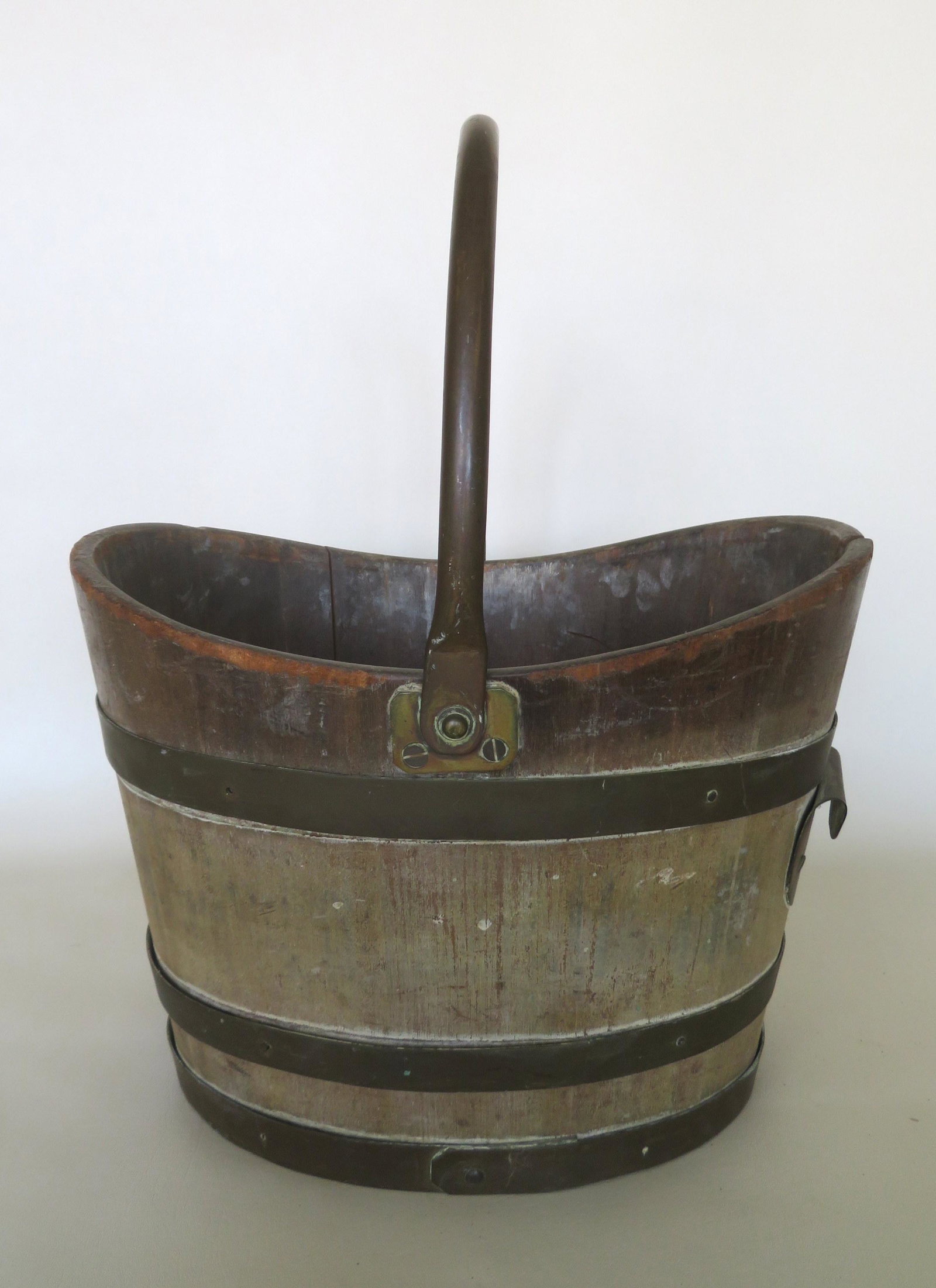 An English brass bound wooden peat moss bucket with: An English brass bound wooden peat moss bucket with curved rim, tubular copper swing handle, and brass grip for pouring and likely hollowed out from a log as the wood frame is all 1 piece of wood with
