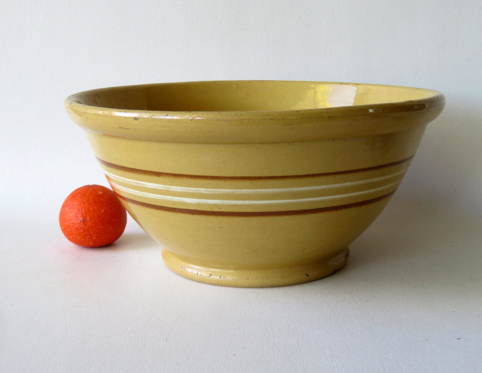 A large yellowware mixing bowl with brown and white: A large yellowware mixing bowl with brown and white rings and rounded rim on footed base, 19th century. 14 1/2"D x 7"H. Very good condition, no damage.