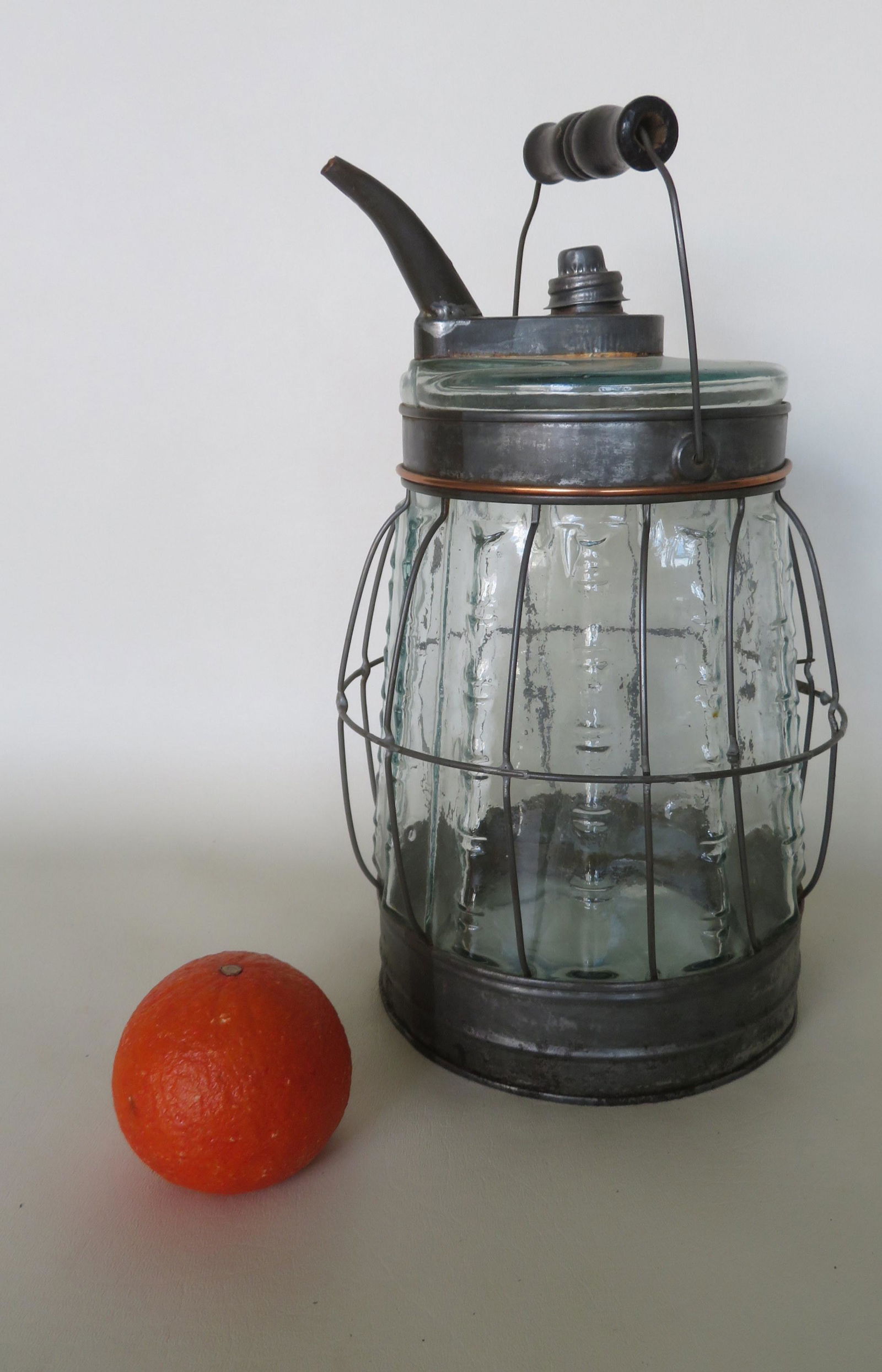 Two near matching kerosene refill bottles with tin lids: Two near matching kerosene refill bottles with tin lids and base, bale handles, and wire cage protector around molded blown glass bottle with embossed decoration, early to mid 19th century. One bottle