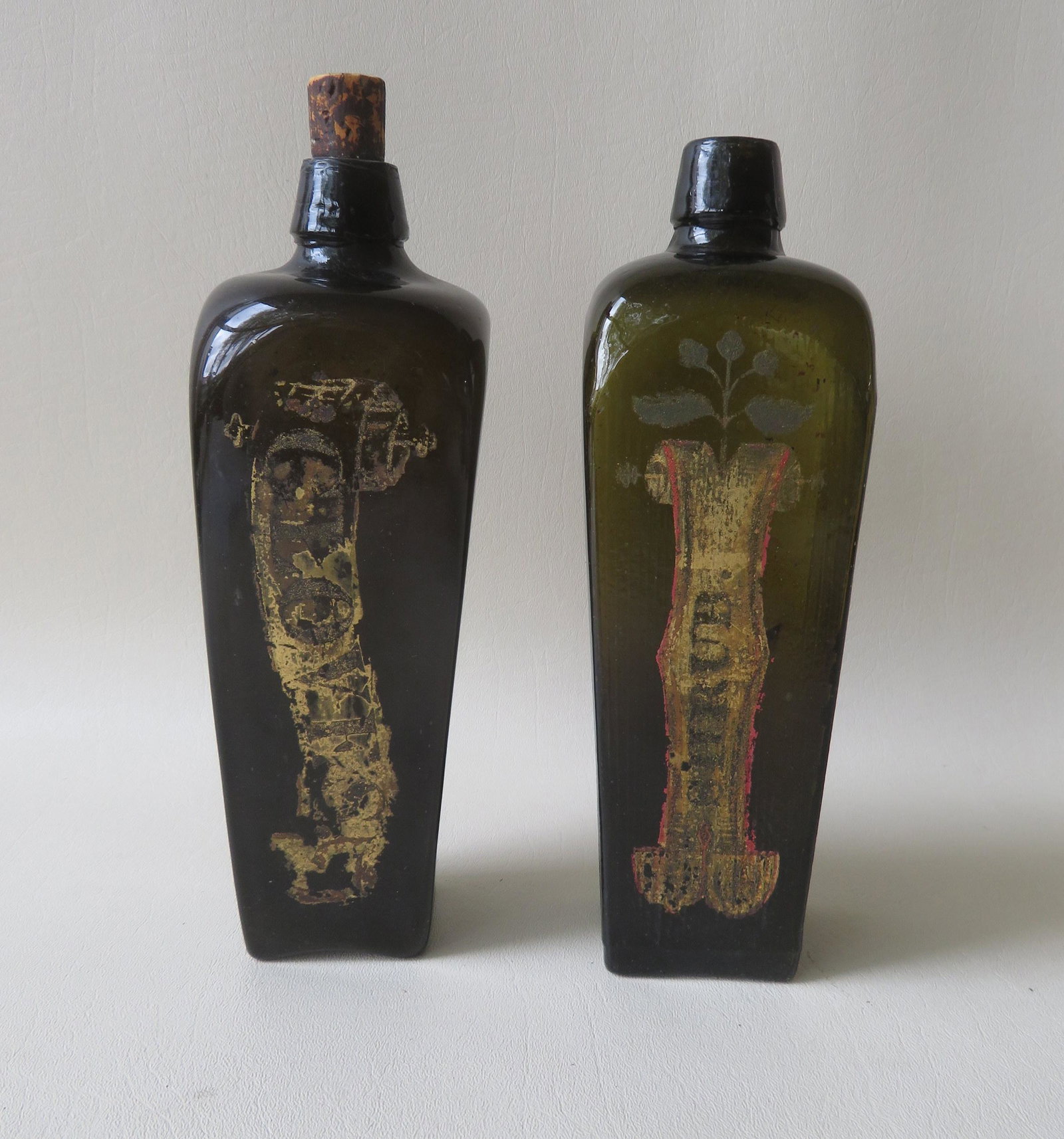 Two unusual olive green cased gin bottles that appear: Two unusual olive green cased gin bottles that appear to have been converted for apothecary use, including one with corrugated body and both with applied lips. Note the hand painted decorations on sid