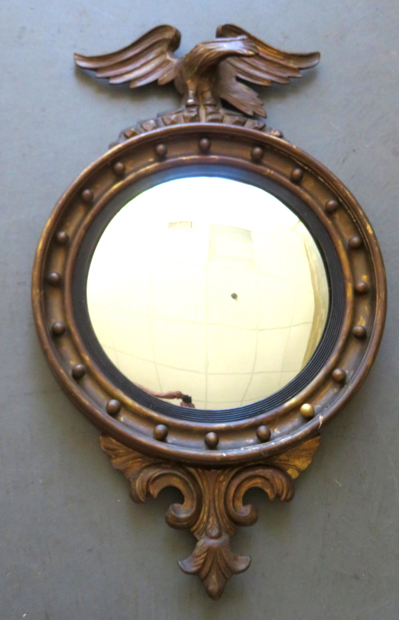 A large bull's-eye mirror having a spread wing eagle: A large bull's-eye mirror having a spread wing eagle finial and scrolled decoration extending from base, probably second period, late 19th century. Original gilt gesso frame with repairs - see photos 