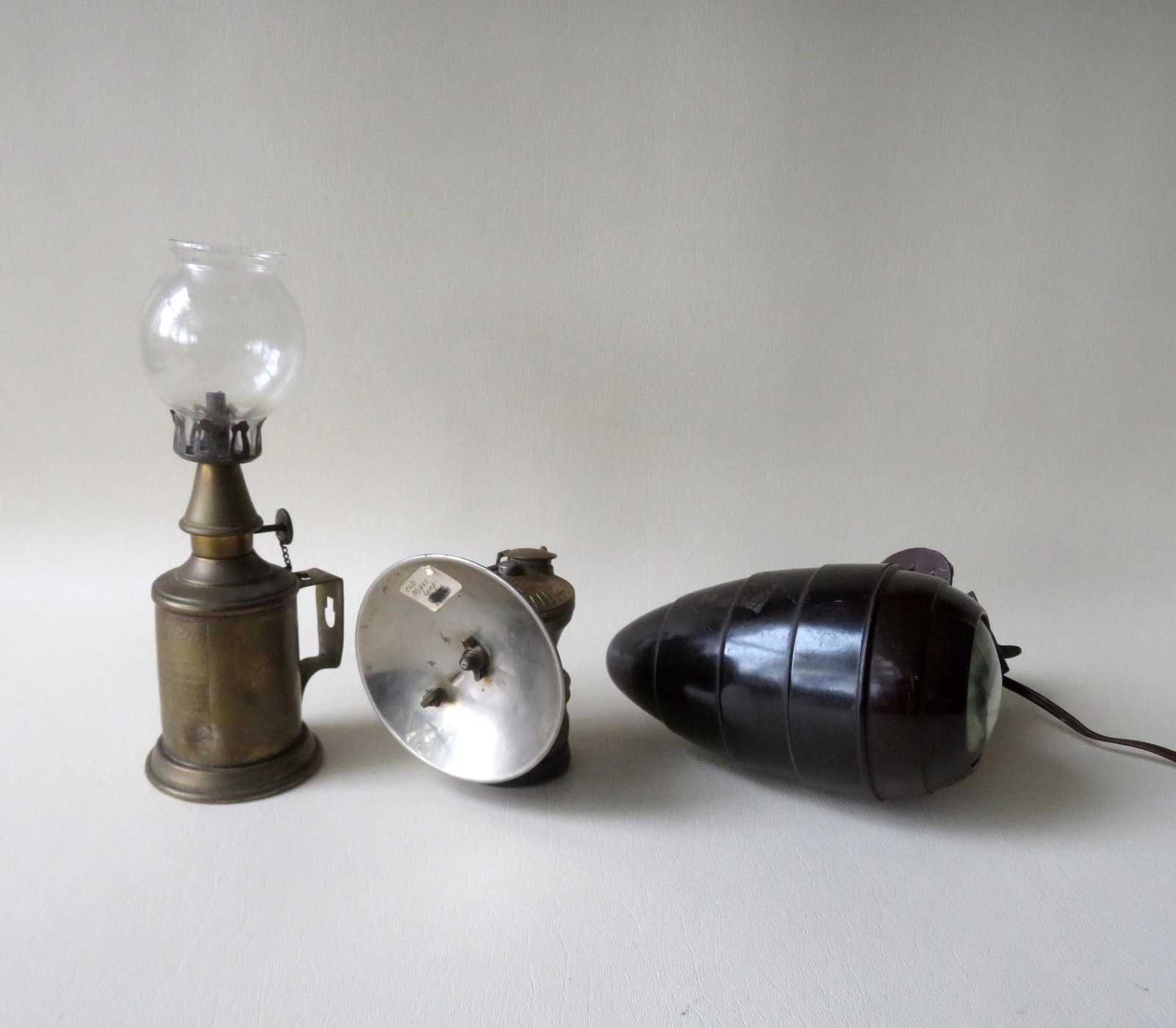 Three various lighting devices including minors lamp, a: Three various lighting devices including minors lamp, a plastic bullet shaped electric light with chain pull on-off switch and mounting bracket, and a French fluid lamp marked Lampe Pigeon on plaque a