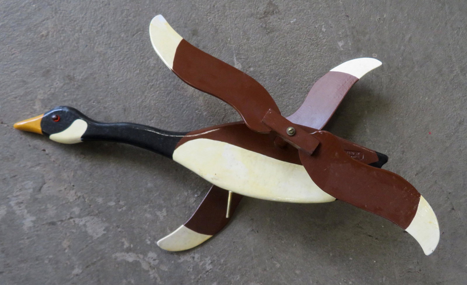 A carved wooden goose whirligig in original paint with: A carved wooden goose whirligig in original paint with glass eyes - impressed maker's name "Hand Crafted by Harry W. Fennell" - very good condition - measures 24 1/2"L to top of wing and 6 1/4"H.