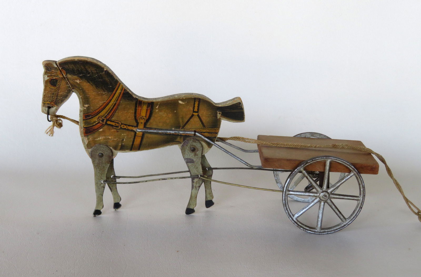 A lithographed horse and wagon pull toy with: A lithographed horse and wagon pull toy with articulated legs. The legs move as the toy is pulled forward. Some use wear to the paper lithograph, but overall good condition. 19th century. 12 1/4"L x 4