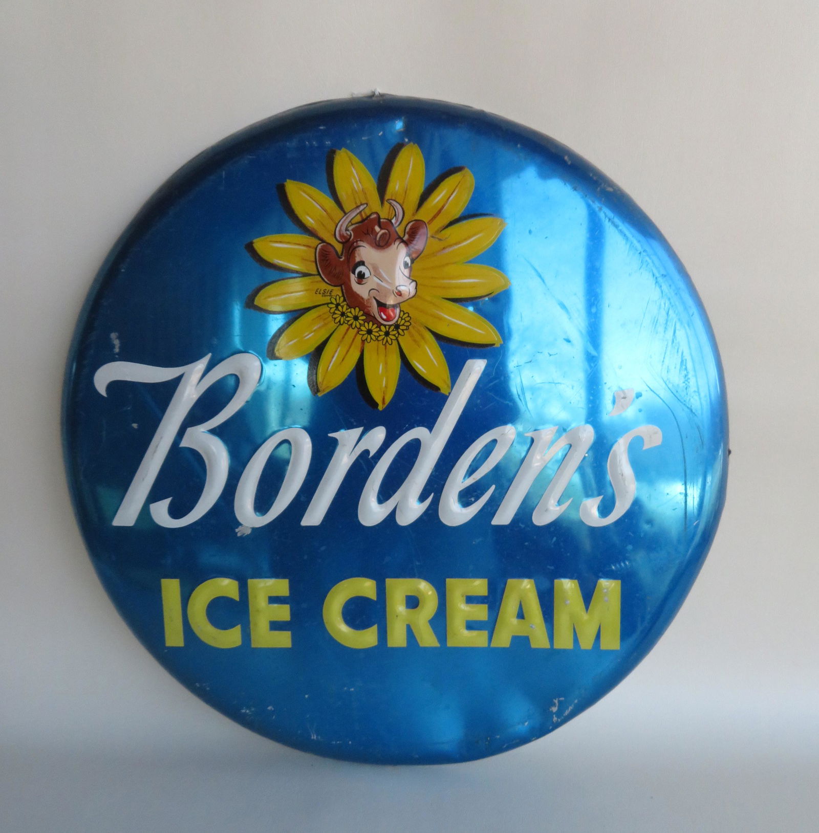 An aluminum "Borden's Ice Cream" button sign with: An aluminum "Borden's Ice Cream" button sign with embossed image of Elsie The Cow, circa 1960. Some surface scratches, minor worn spots, 2 dents near bottom edge, overall good condition. 24" diameter.