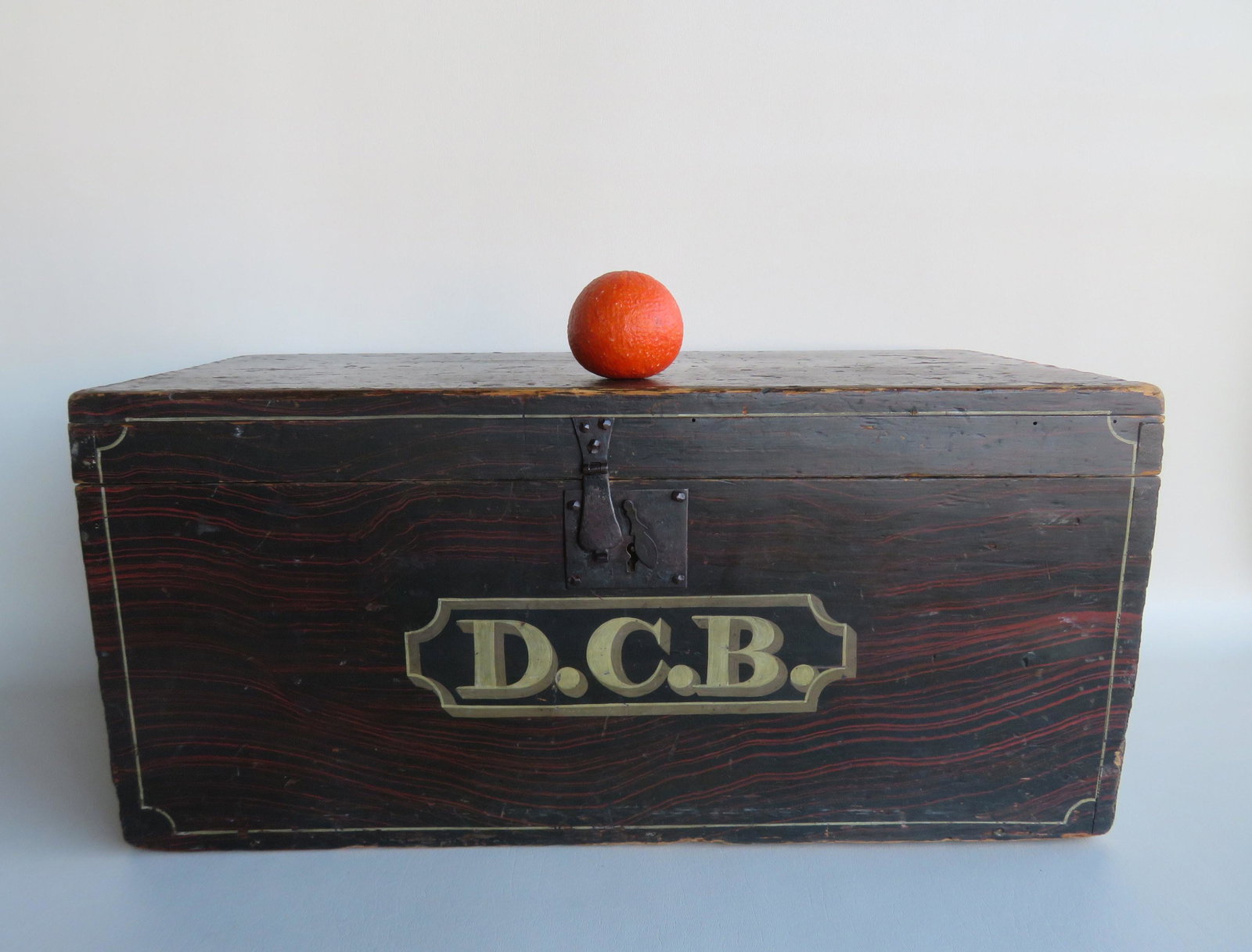 Grain painted storage box in original red and black: Grain painted storage box in original red and black paint with white pin striping and signed across the front with gray and white shadow lettering "D.C.B." - iron hasp, lock and handles which are orig