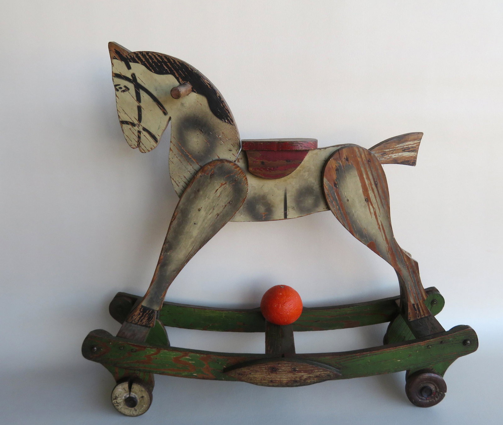 A child's hand painted and stenciled rocking horse: A child's hand painted and stenciled rocking horse riding toy on wheels - original paint - circa 1900. The wheels with shrinkage cracks, slight use wear, and overall good condition. 23"L x 8"W x 20"H.