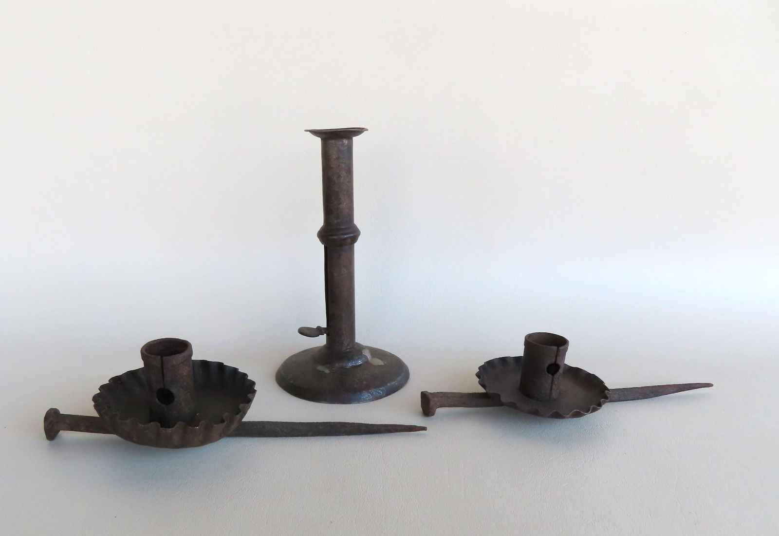 Three early metal lighting devices including 2 sticking: Three early metal lighting devices including 2 sticking tommies with candle holders - 8 1/2"L x 2"H, and 1 hog scraper candlestick with wedding ring - 7 1/4"H. All very good condition.