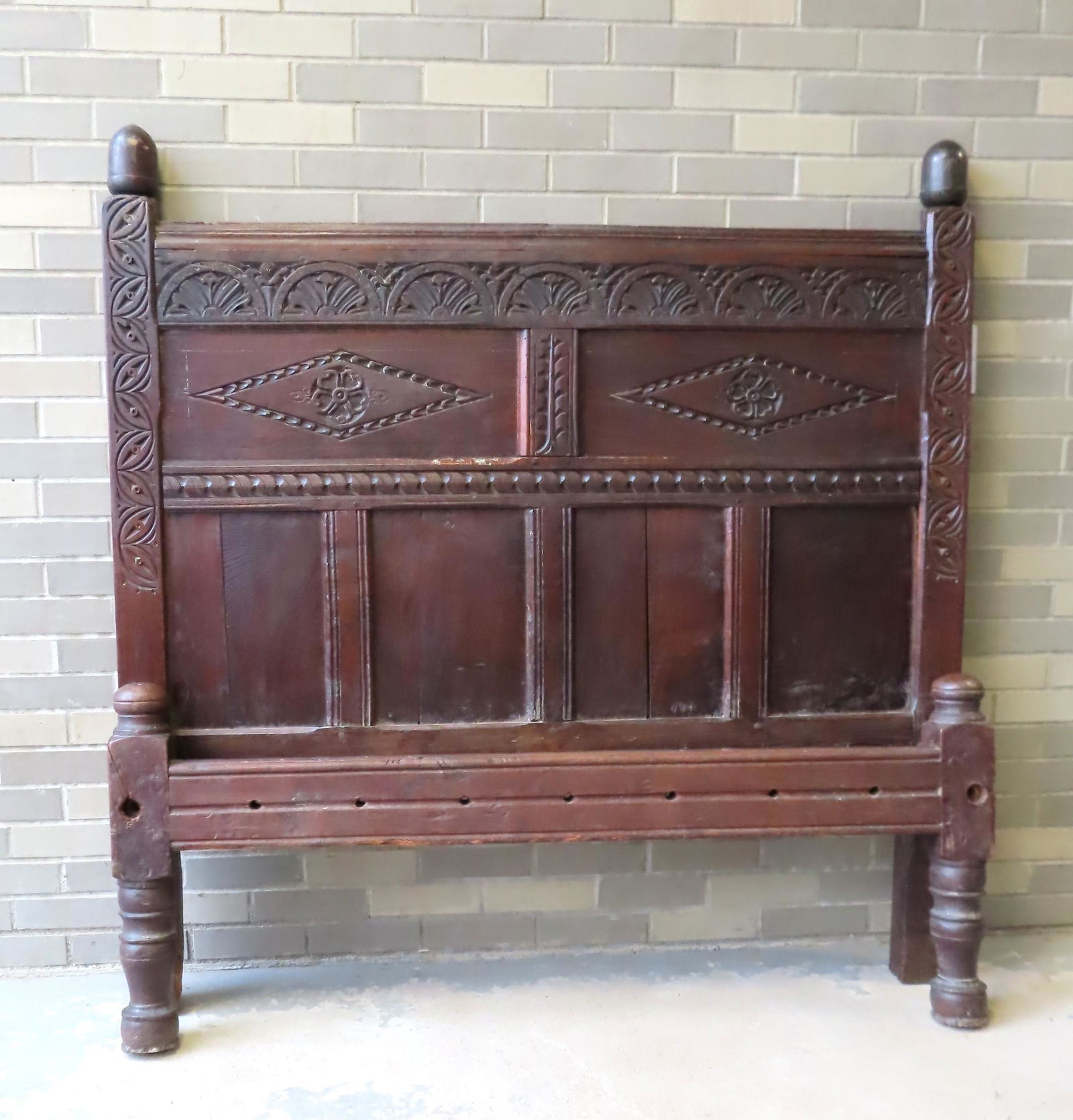 A Jacobean paneled bed in oak, having a top panel: A Jacobean paneled bed in oak, having a top panel decorated with flowers within arches over 2 carved panels with a flower within diamond, over 4 oak panels, and having scrolled carvings down posts, ci