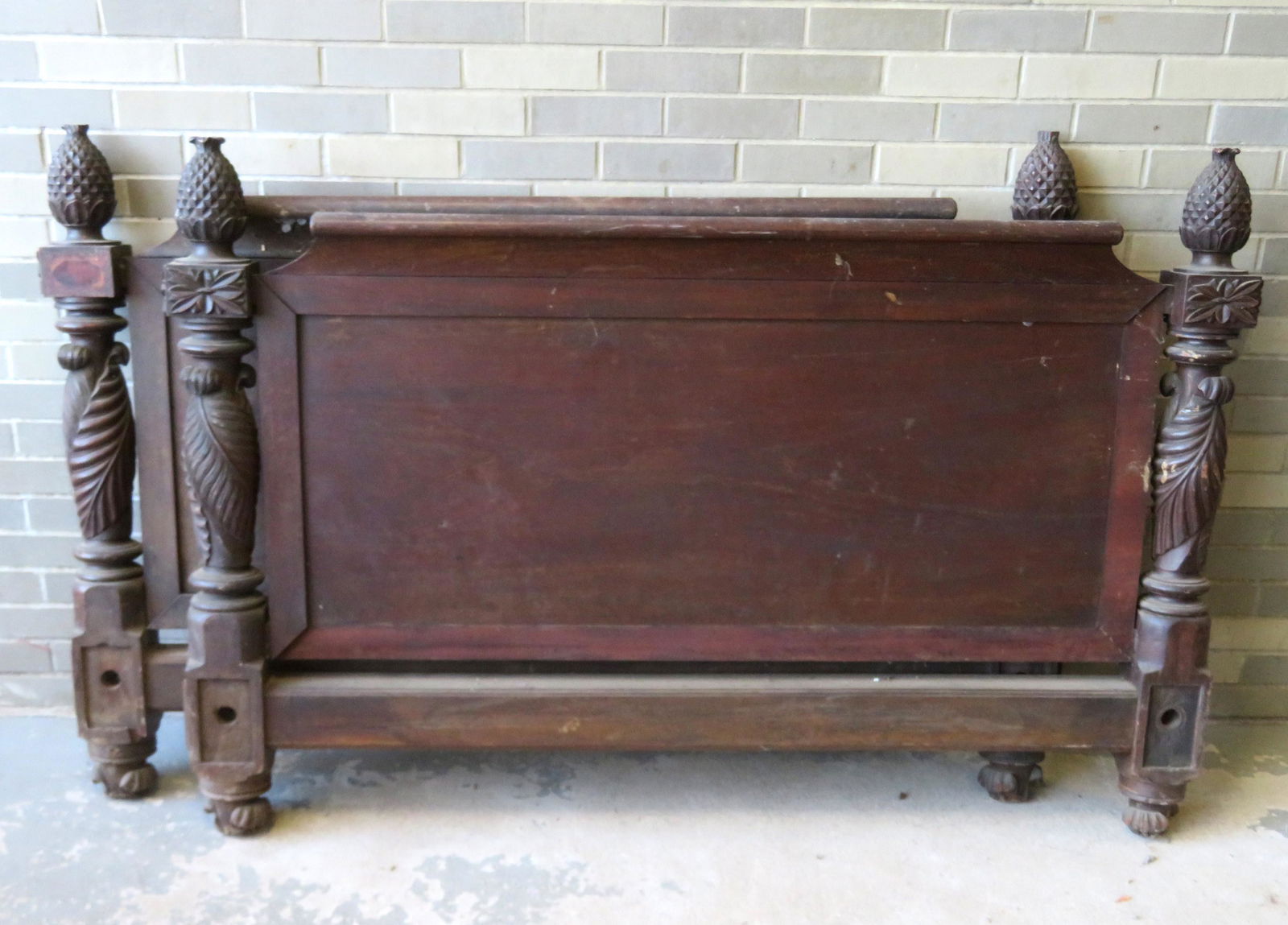An early mahogany bed with matching pineapple finials: An early mahogany bed with matching pineapple finials on headboard and footboard, and having heavily carved acanthus posts resting on carved feet. Losses to top of pineapples, the crest on headboard i
