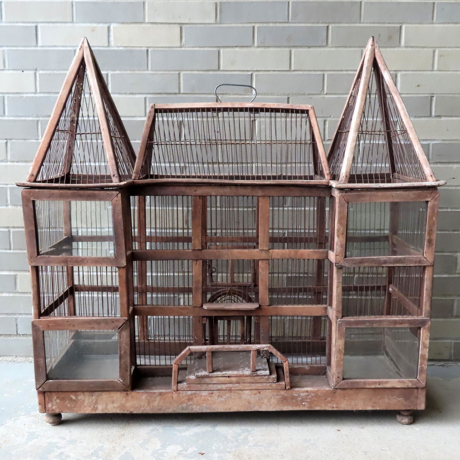 An architectural building shaped wire and wood bird or: An architectural building shaped wire and wood bird or animal cage having a bridge in front of the arched door, and 4 beveled glass windows, with traces of original paint. The bottom tin tray is remov