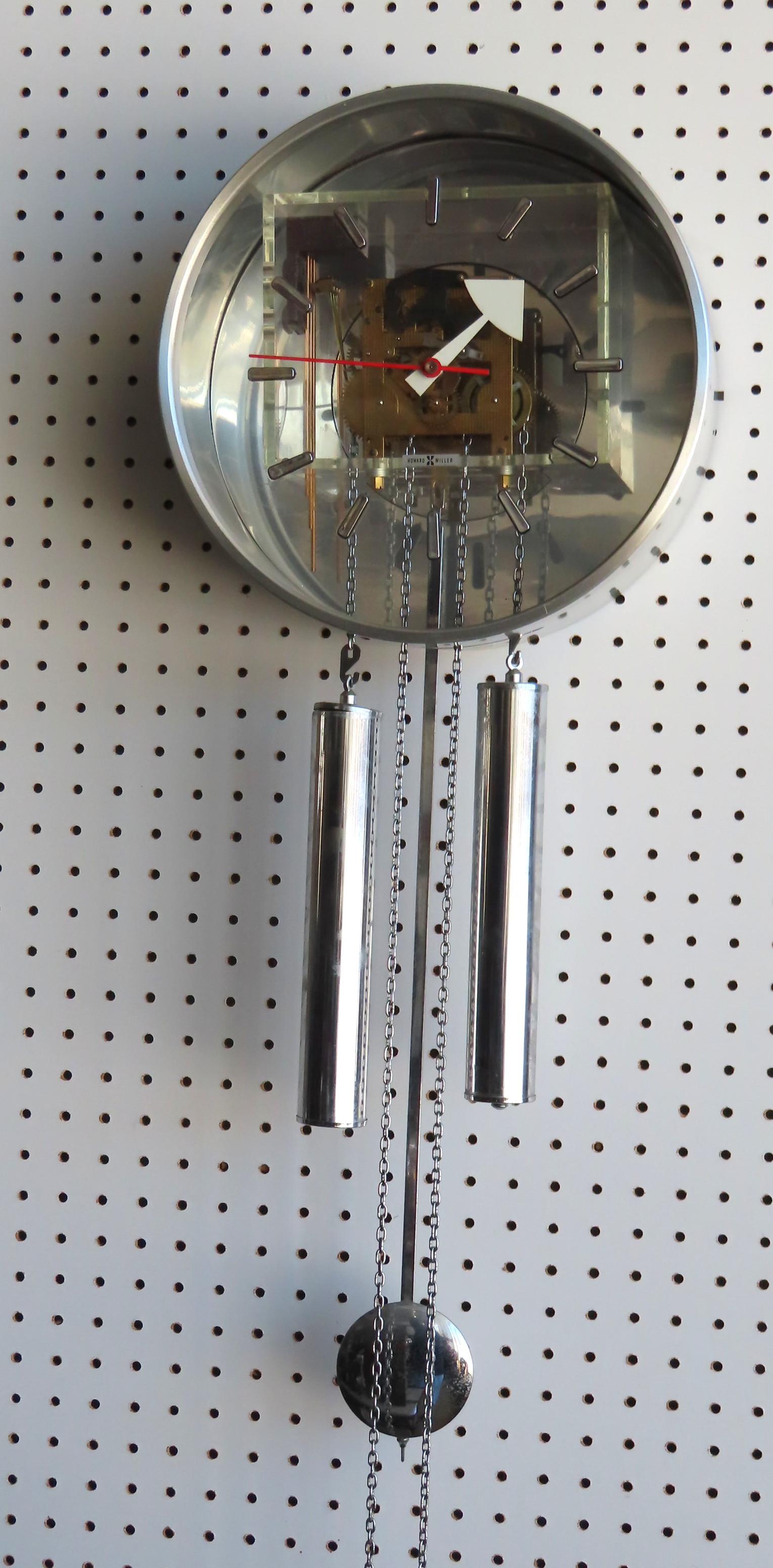 A mid-century modern Howard Miller wall clock designed: A mid-century modern Howard Miller wall clock designed by George Nelson, having a transparent Lucite face , open works mounted on Lucite platform, mirror back, polished aluminum case, long drop chrome