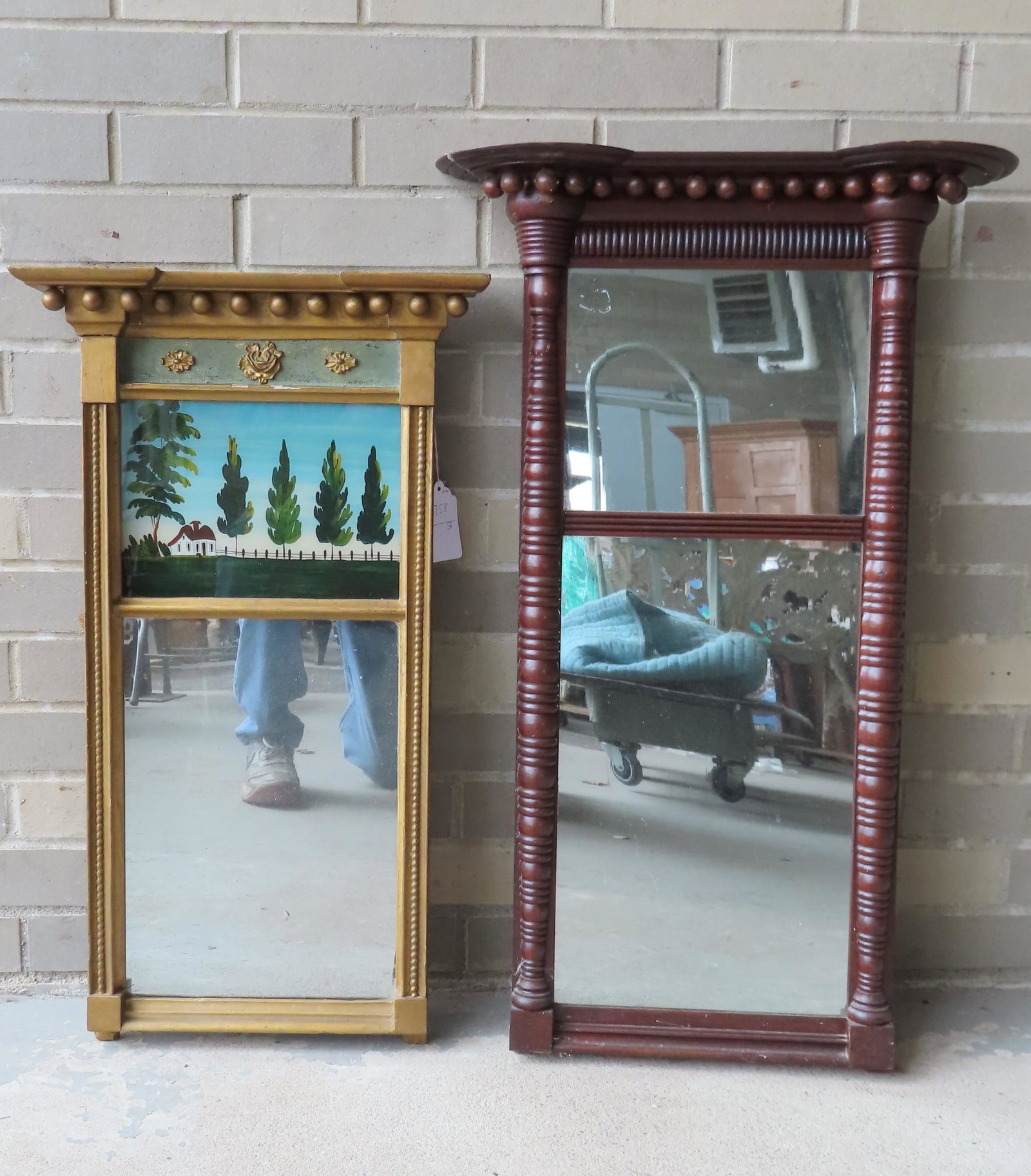 Two Sheraton wall mirrors including: A 2 part gilded: Two Sheraton wall mirrors including: A 2 part gilded mirror with shaped crest over a gesso panel with a green painted ground over an eglomise panel depicting a row of evergreen trees and fencing leadi