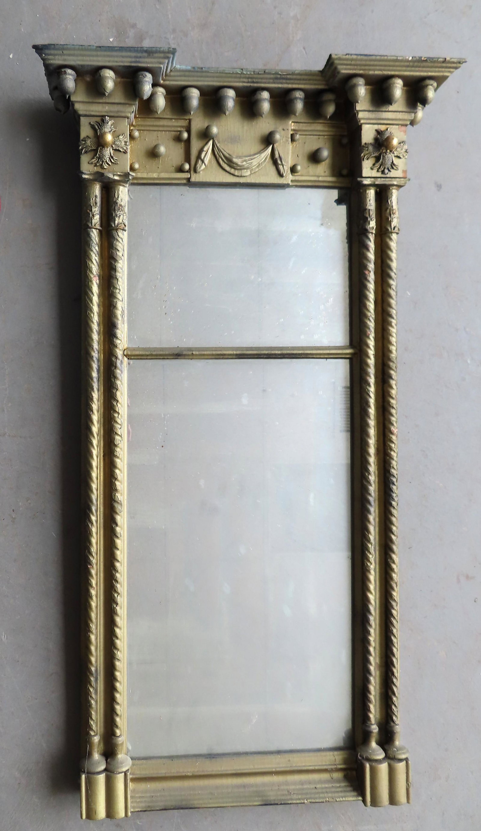 A double panel Sheraton wall mirror in gilded gesso: A double panel Sheraton wall mirror in gilded gesso having a shaped top with hanging acorns over a panel decorated with a central swag, and flanked by stylized corner rosettes over double twisted 1/2 