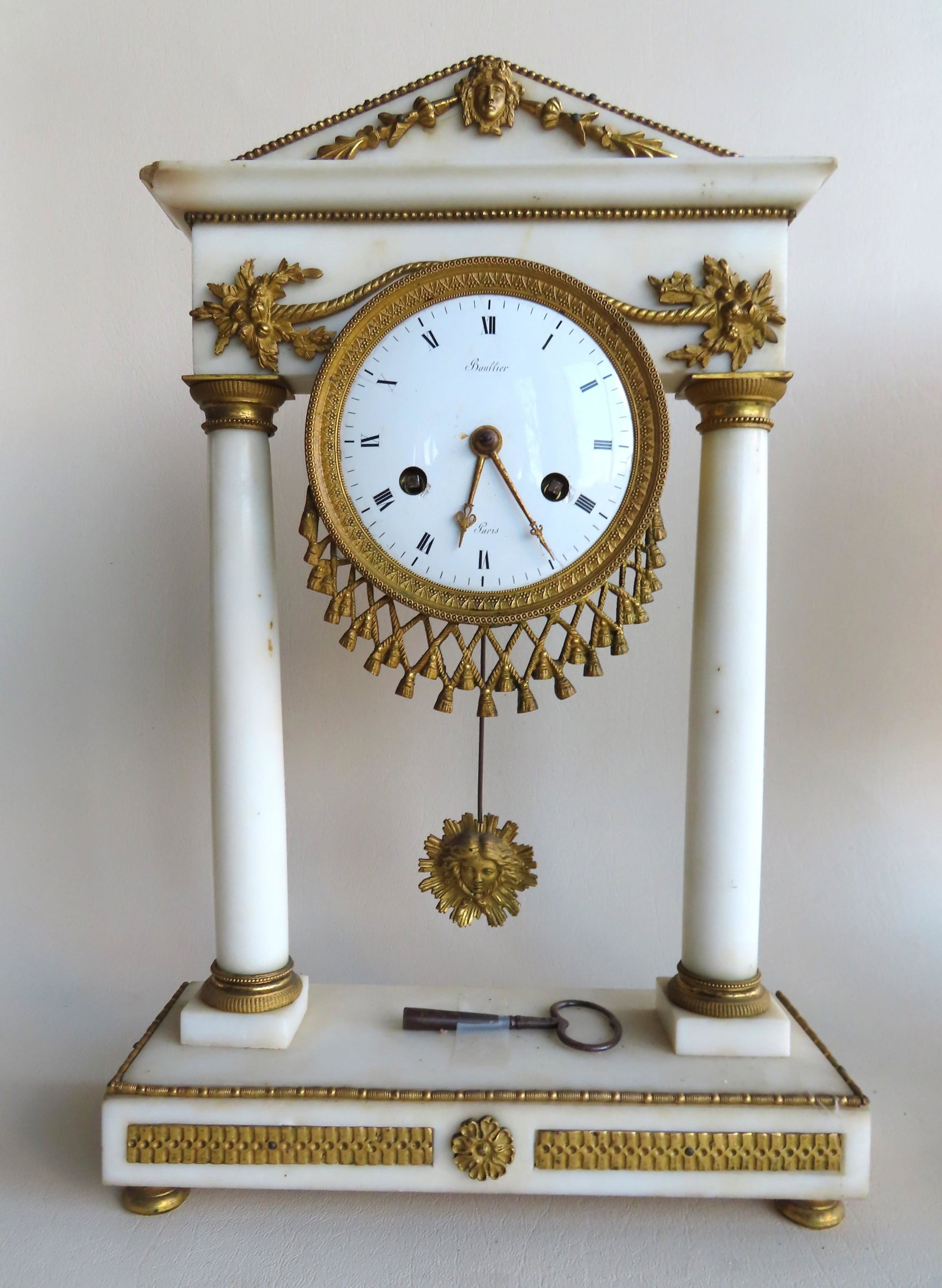 A French Empire white marble mantle clock with applied: A French Empire white marble mantle clock with applied gilt bronze cornucopia plus other ormolu, early 19th century, signed on porcelain face "Baullier/Paris". The double columns with gilt bronze capi
