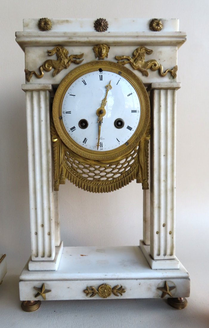 A French Empire white marble mantle clock with applied: A French Empire white marble mantle clock with applied gilt bronze ormolu including 2 Greek mythological figures of a sea-goat (half goat, half fish). The porcelain face signed A'Paris. Four columns s