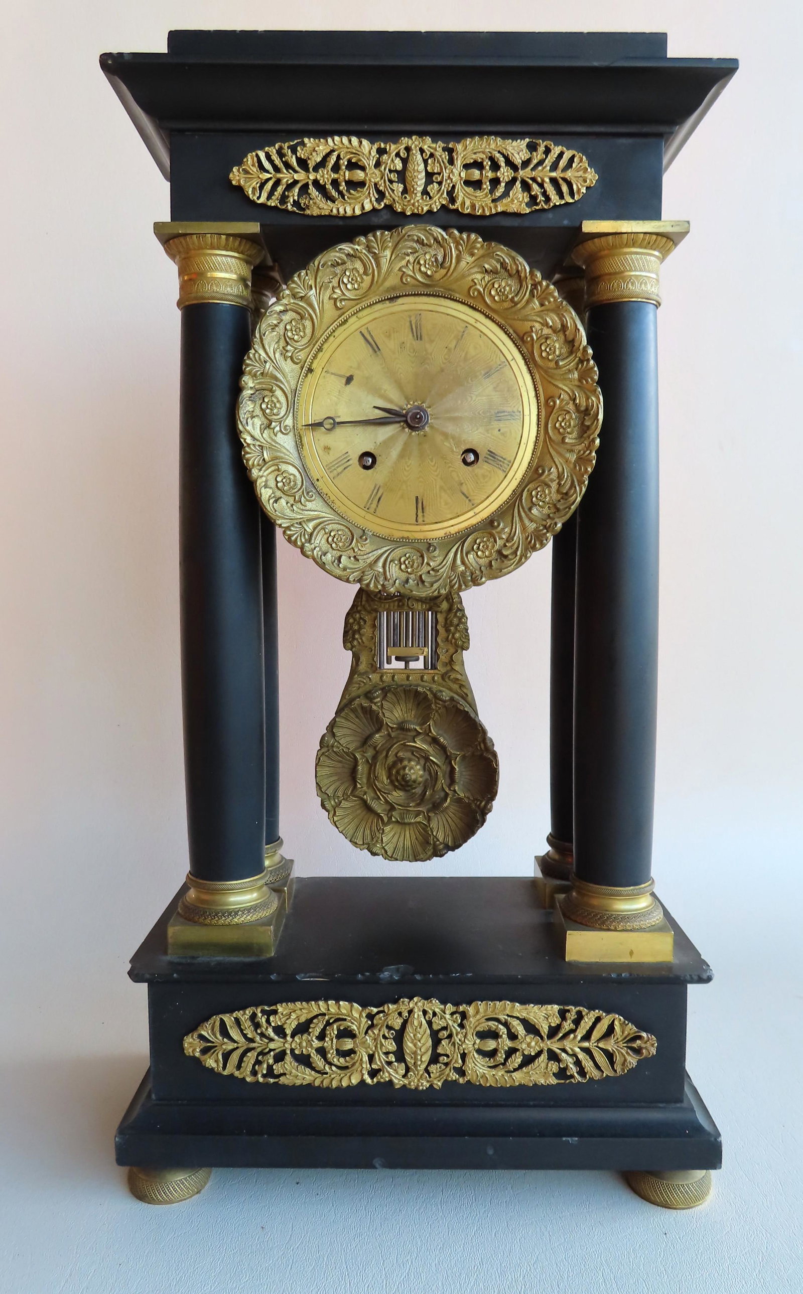 French Empire black marble mantle clock having 4: French Empire black marble mantle clock having 4 columns with gilt bronze capitals and platforms and applied gilded ormolu. The large brass pendulum in the form of a flower. Early to mid 19th century.