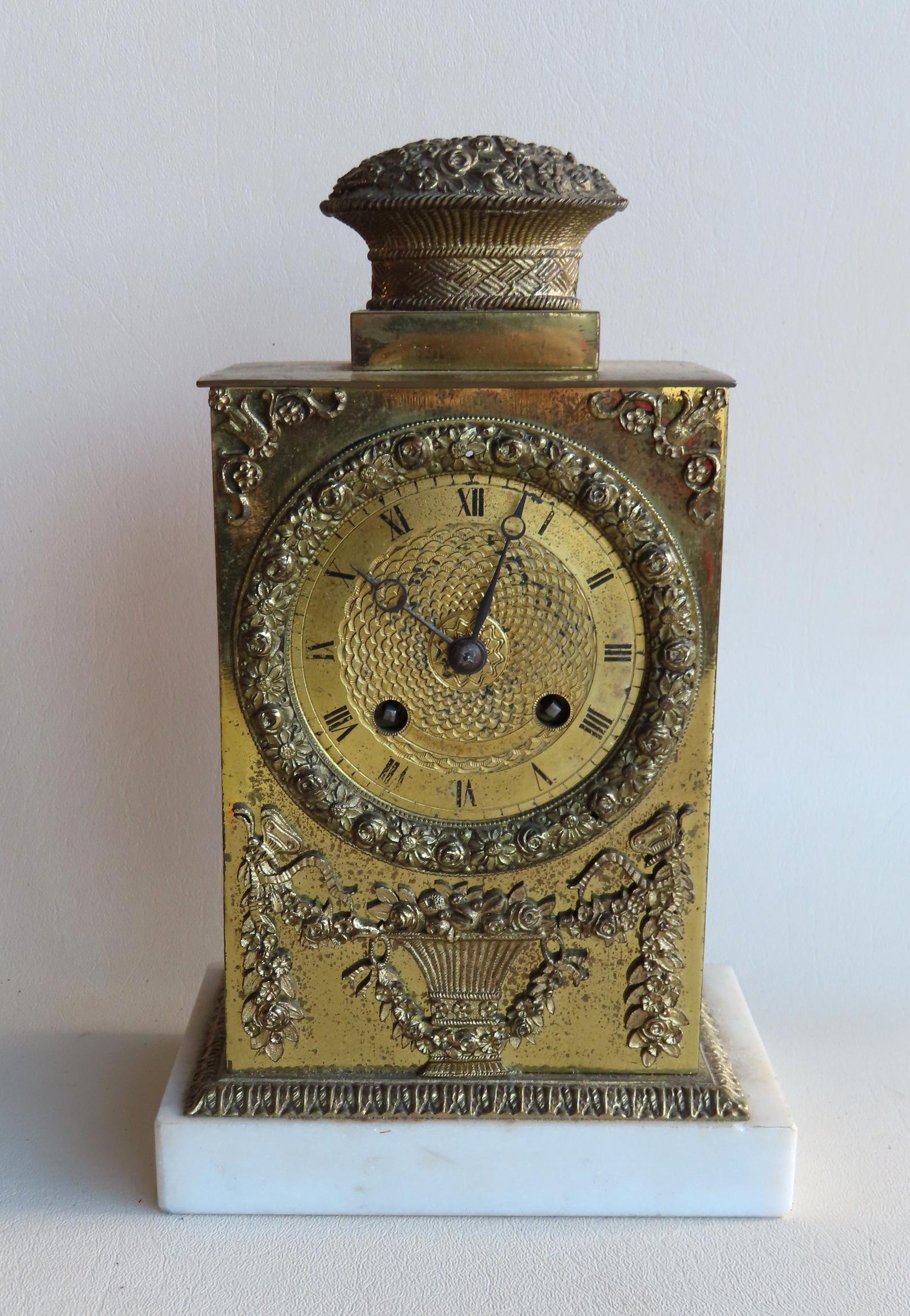 A small French Empire brass dresser clock with windup: A small French Empire brass dresser clock with windup mechanism and having applied brass ormolu including an urn with flowers under clock face - also note the brass basket of flowers mounted on the cl