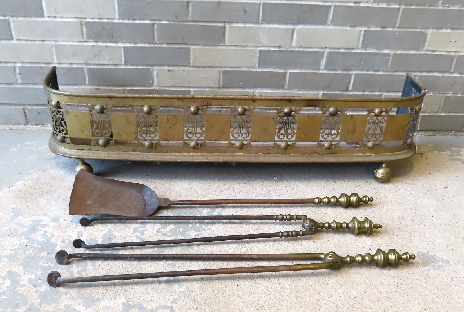 Grouping of 4 early brass hearth items including: A: Grouping of 4 early brass hearth items including: A fireplace fender, the front with openwork lyre decorations surrounded by small leaves and base with ball feet, mid to late 19th century - very good 