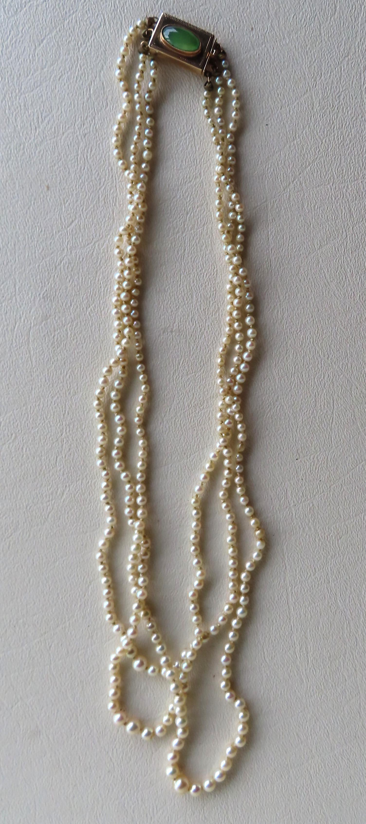 A triple strand pearl necklace attached to a 14K gold: A triple strand pearl necklace attached to a 14K gold rectangular clasp with a jade colored stone. As it hangs from the neck to the back of the clasp, it measures 10 3/4"L - the clasp mark 14k and mea