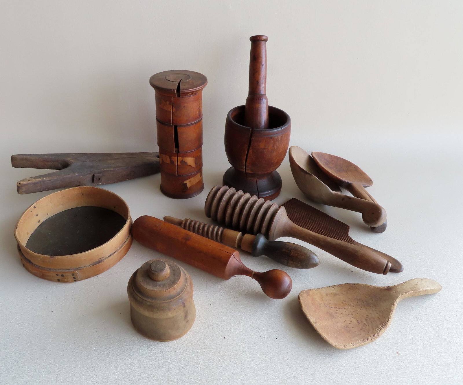 A grouping of country treenware primitives.: A grouping of country treenware including: Mortar and pestle (expansion crack in mortar), various wooden mashers, a sieve, primitive wooden boot jack, 3 butter paddle/scoops & scoop (one in birdseye m