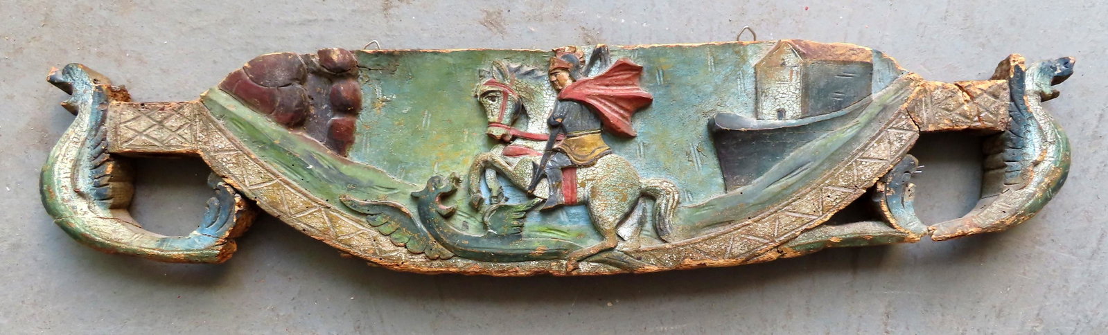 A carved wooden ornament from a 18th/19th century: A carved wooden ornament from a 18th/19th century Italian goat card depicting St. George and the Dragon flanked by carved stylized dolphins in the corners - all original polychrome paint. Some wear an
