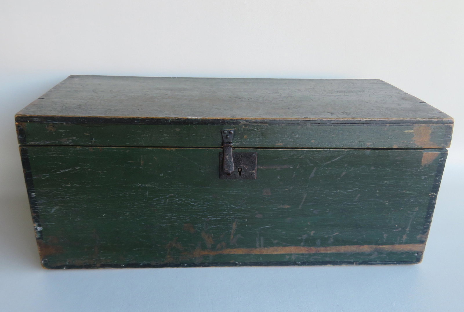 A storage box in original green paint with black pin: A storage box in original green paint with black pin striping and initialed "M A W" in the center of the lid, original green paint with iron hasp and lock, early 19th century. The box measures 23 1/2"