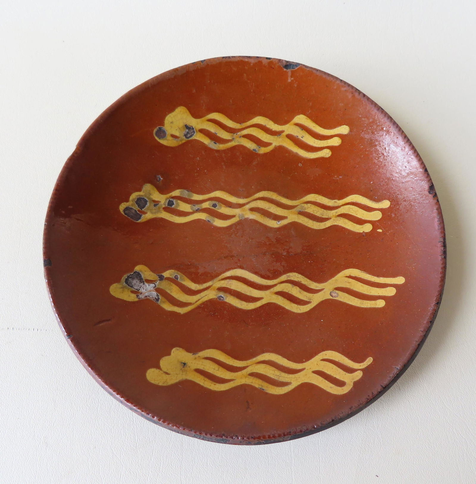 Redware plate with yellow slip decoration in the form: Redware plate with yellow slip decoration in the form of 4 groups of 3 squiggle lines, and having a slight coggled edge, 19th century - 10 1/4" diameter. Minor use wear to plate interior, minor rim ch