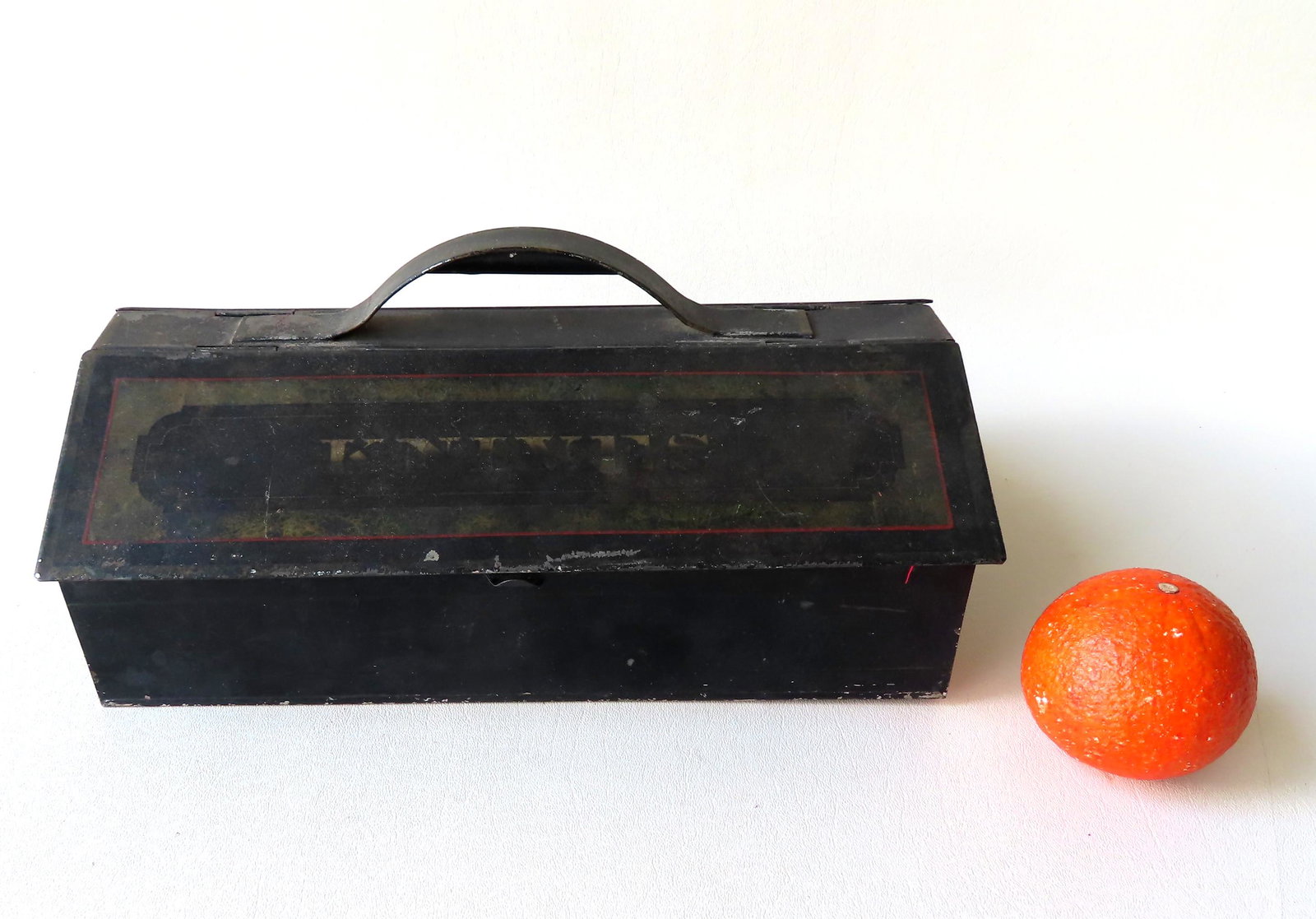 A toleware cutlery box in original paint having a domed: A toleware cutlery box in original paint having a domed tin handle separating to compartments containing "FORKS" and "KNIVES". Some wear to paint, but overall good condition. Measures 13 1/4"W x 8"D x