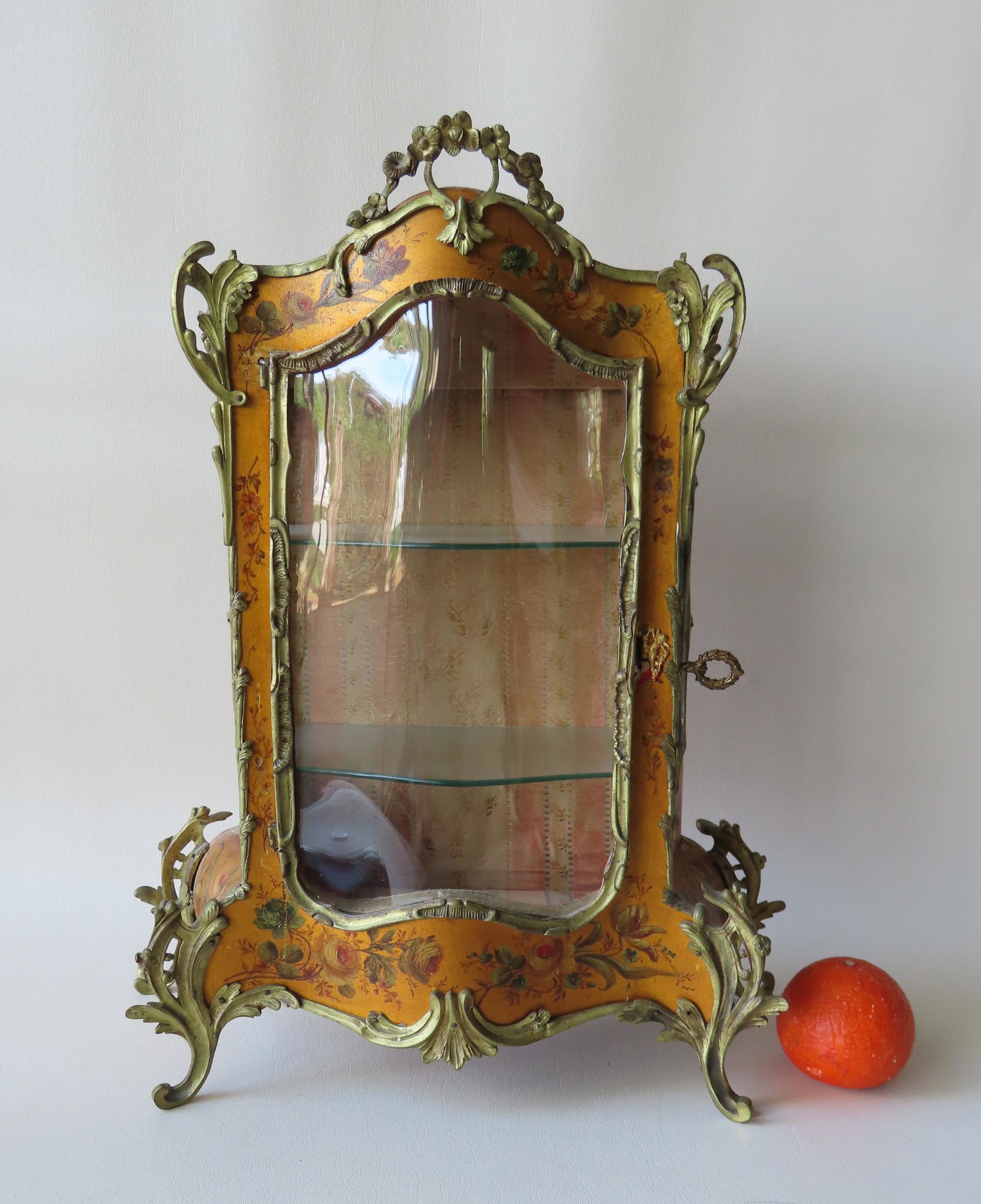 A small fancy hand painted French table top vitrine: A small fancy hand painted French table top vitrine with a serpentine glass front, concave glass sides, original painted floral surface over gilding, and applied gilt bronze ormolu on crest and acanth