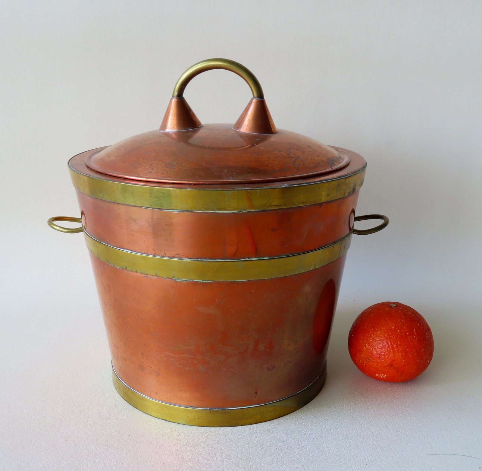 A mid-century James Casey copper ice bucket having: A mid-century James Casey copper ice bucket having double handles and with monogram "JC" on base which is also stamped "Hand Made". Exterior in copper with brass straps and interior stainless steel. V