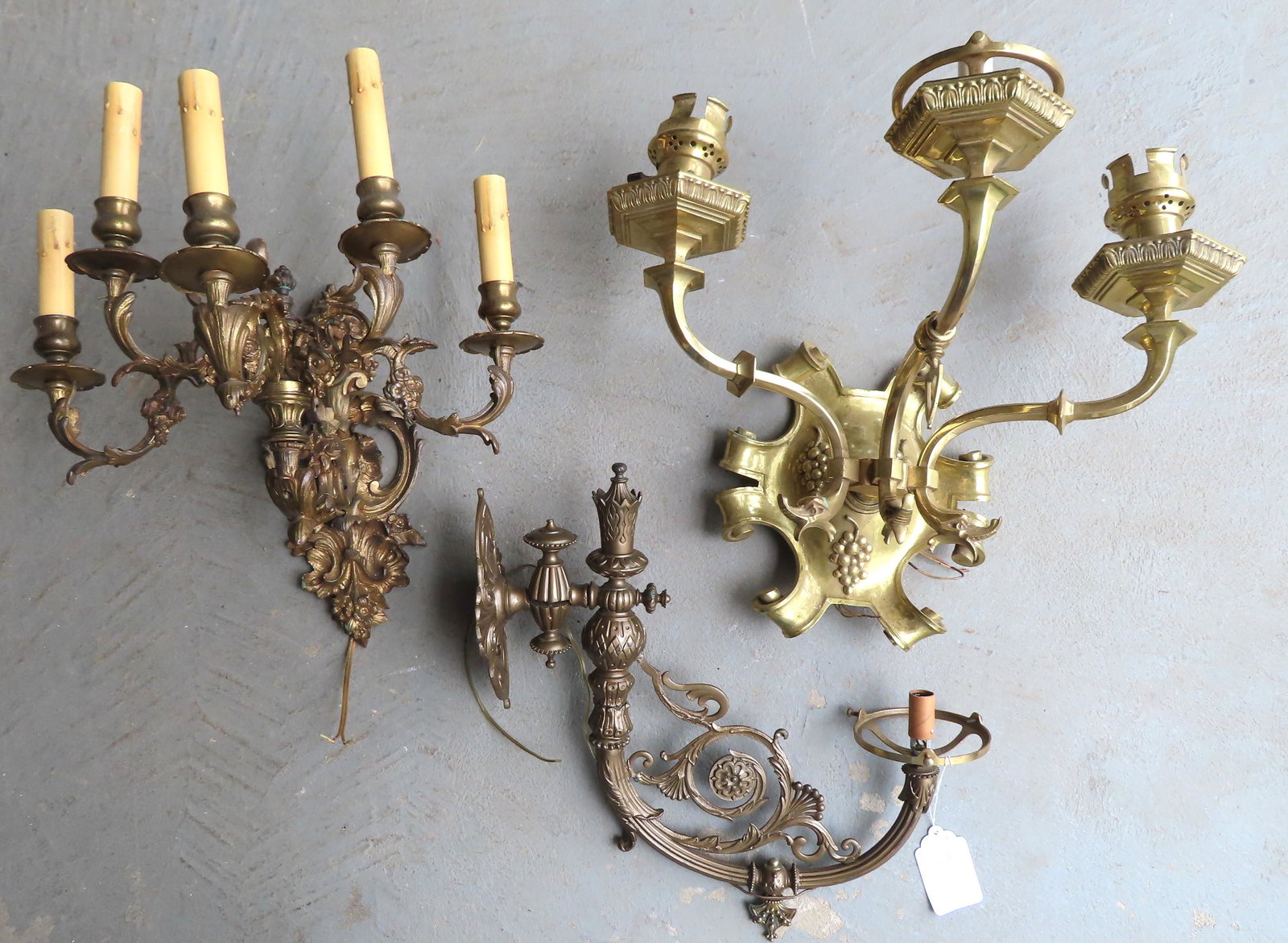 Three metal electrified wall sconces including: A very: Three metal electrified wall sconces including: A very fine heavy brass 3 light sconce with dolphin form terminals on the arms and having a scrolled back-plate decorated with embossed grapes - no shad