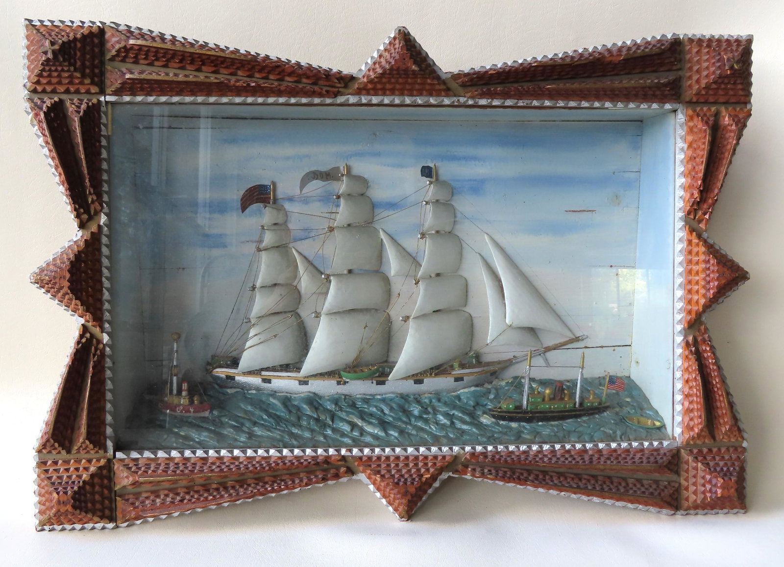 The best nautical diorama depicting a hand carved 3: The best nautical diorama depicting a hand carved 3 mast schooner bearing an American flag, flanked by 2 smaller steamboats, all in original paint. It is mounted in it's original outstanding tramp art