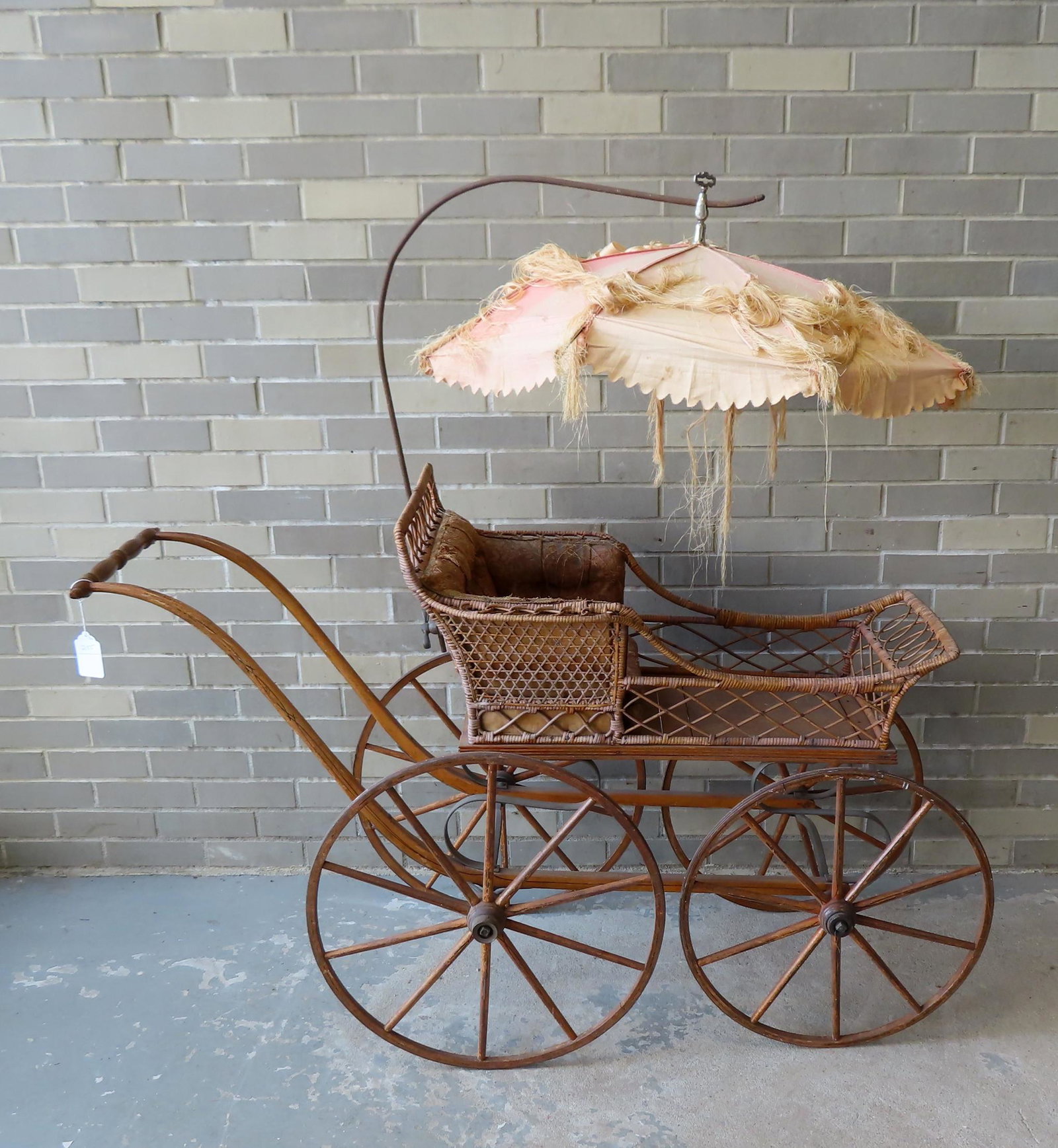 A good wicker baby stroller with removable and: A good wicker baby stroller with removable and adjustable parasol. The carriage with wooden wheels, original upholstered seat (wear and losses), and original pin striping on curved arms leading to han